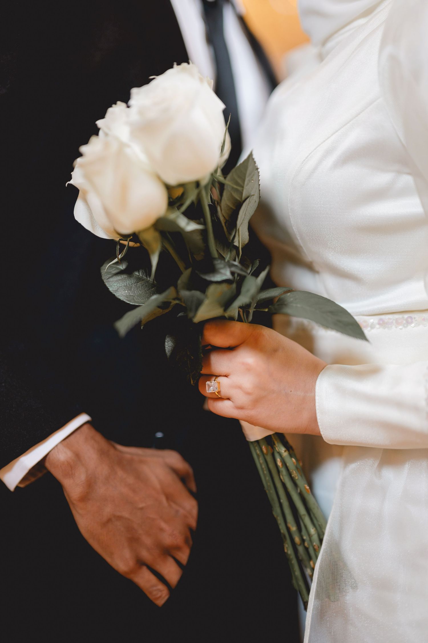 Hands holding a bouquet of white roses against white fabric background.