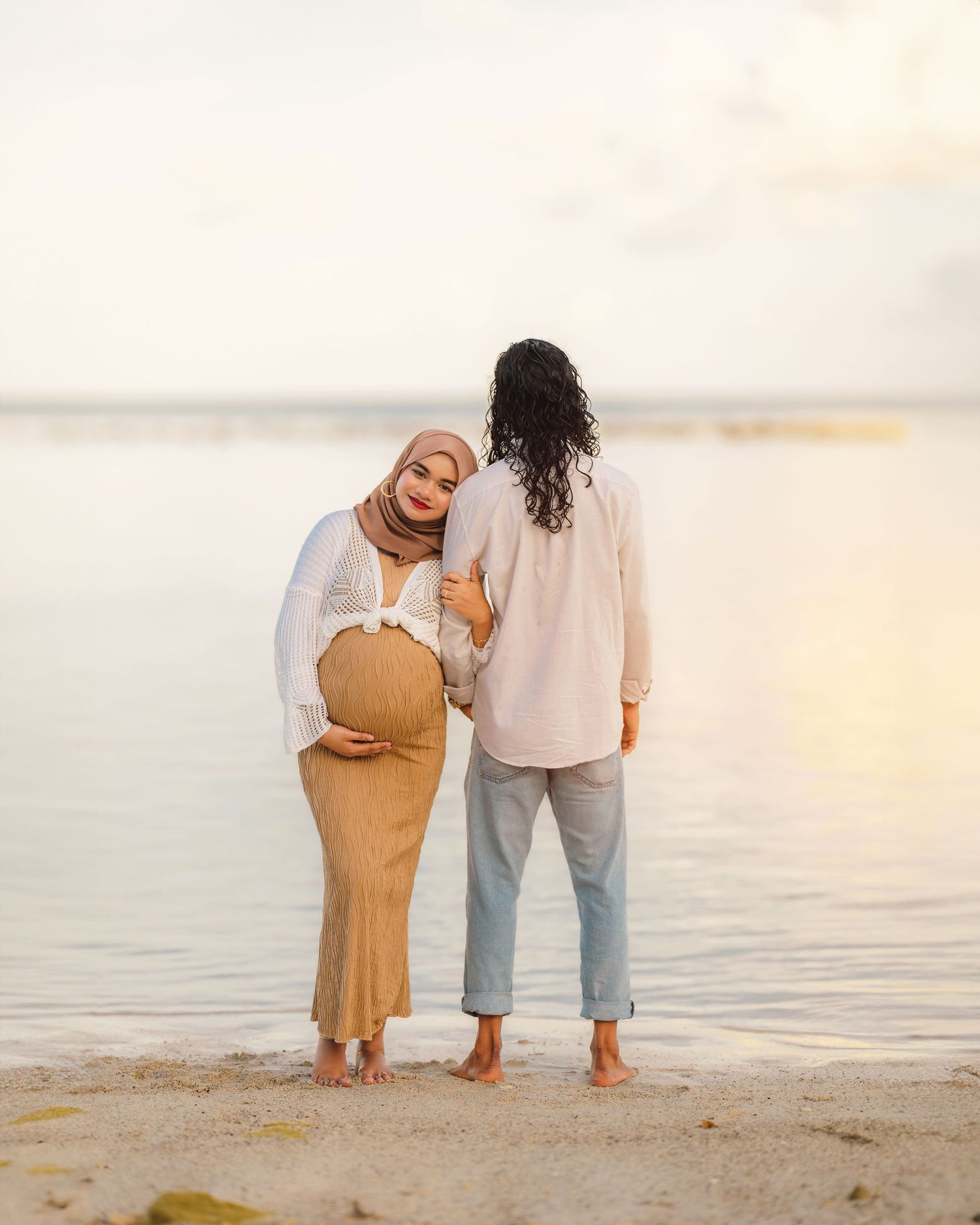 Two people share an intimate moment while standing together on a beach at sunset.