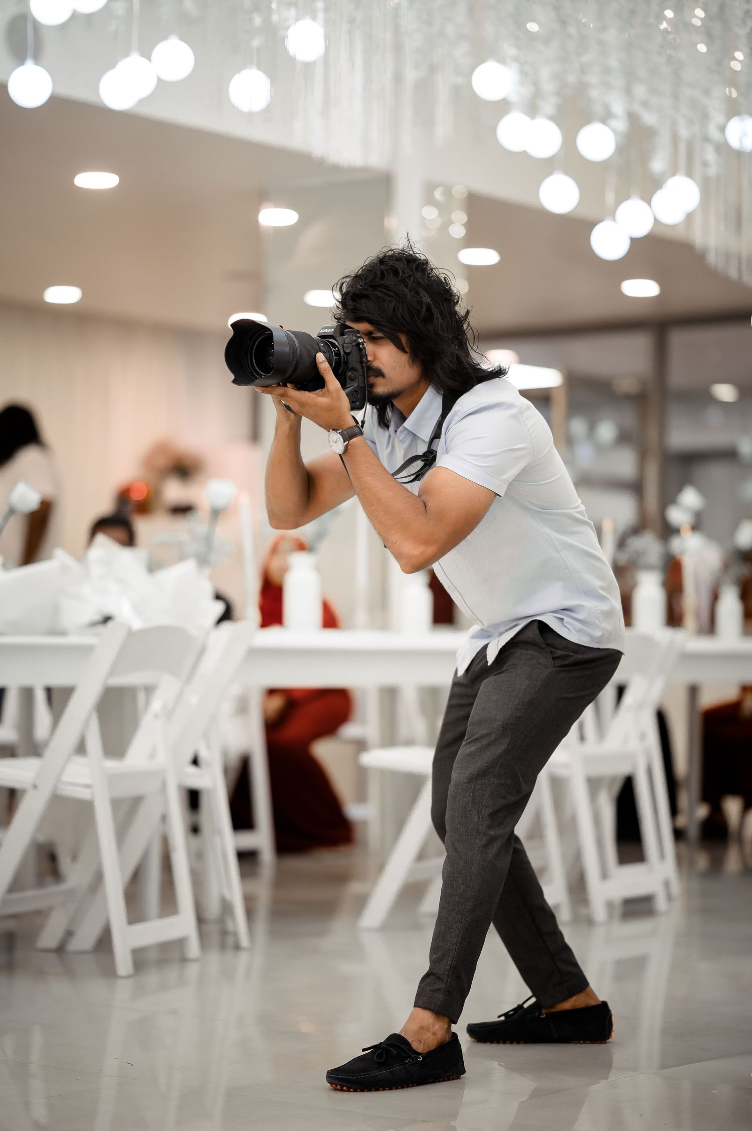Wedding photographer crouching to capture shots in white event space.