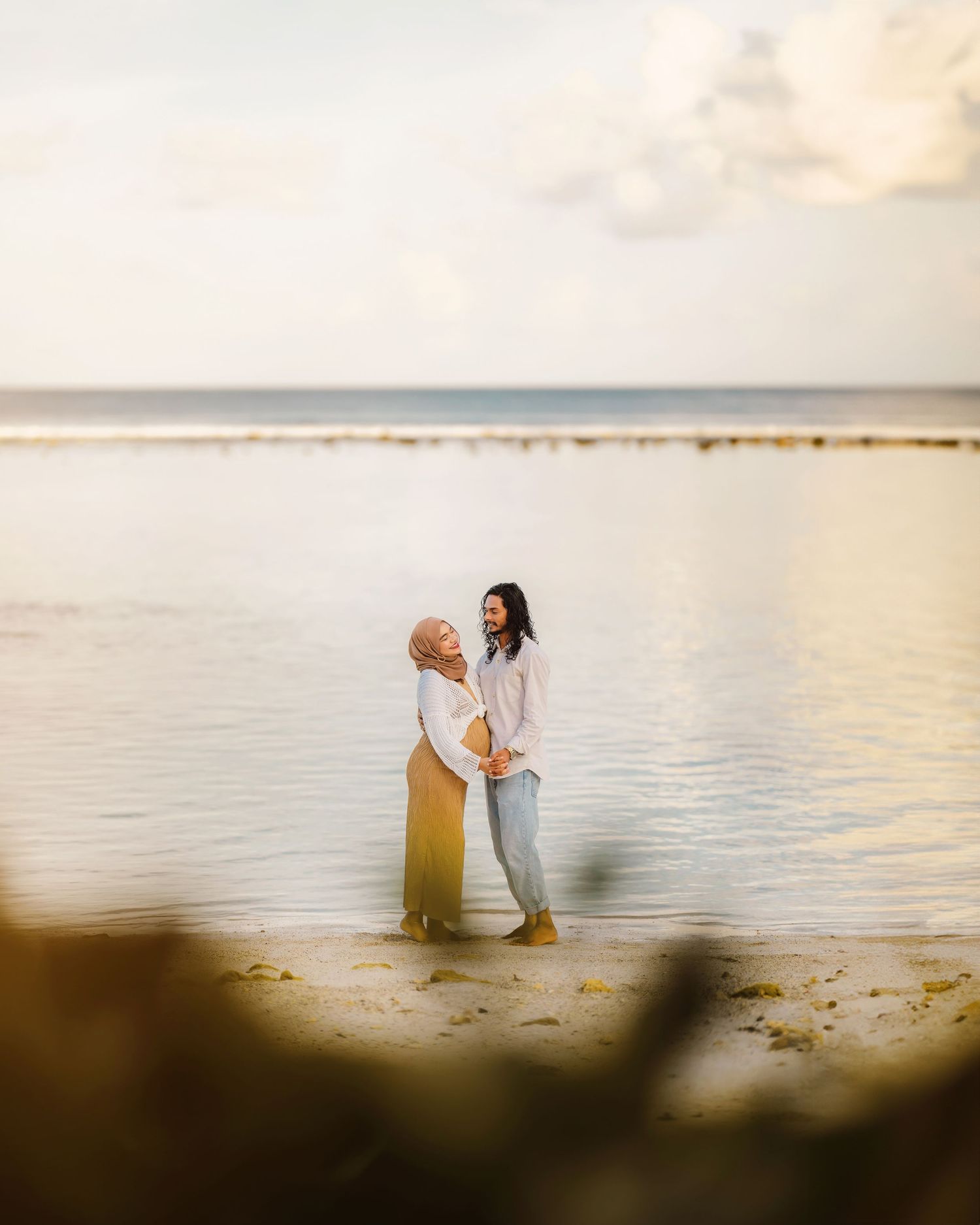 A romantic beach scene with two figures sitting by the ocean during golden hour.