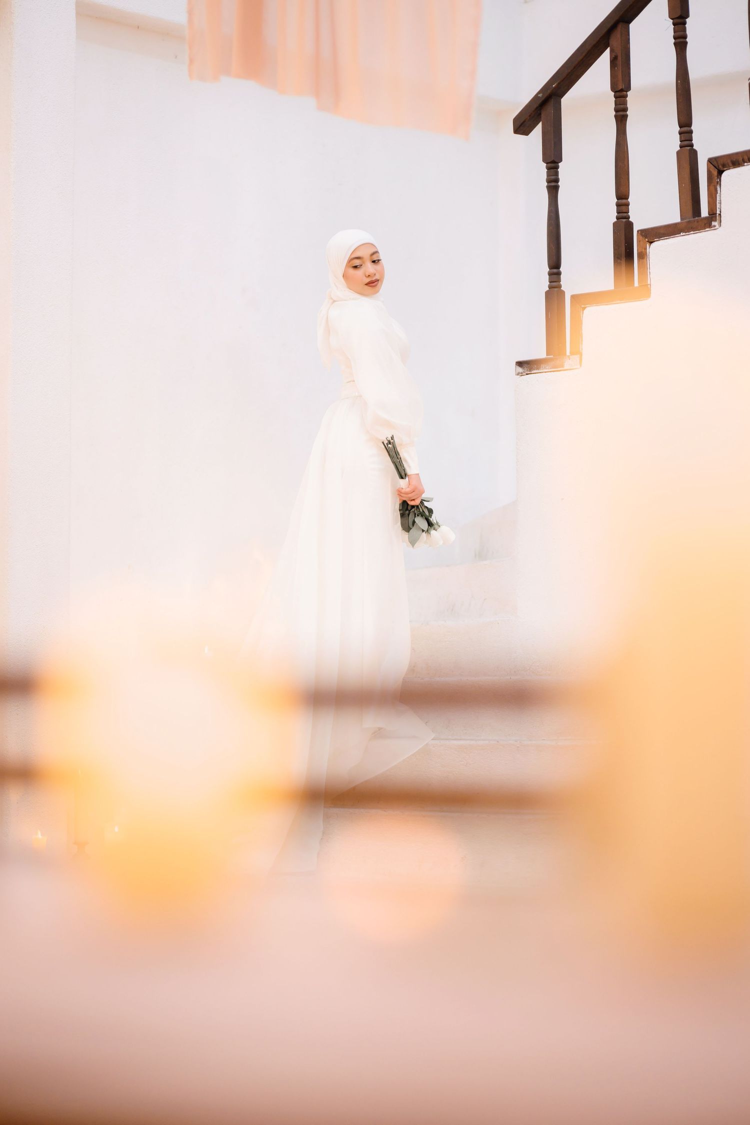 Minimalist wedding photo with soft focus and warm lighting against white walls and wooden railings.