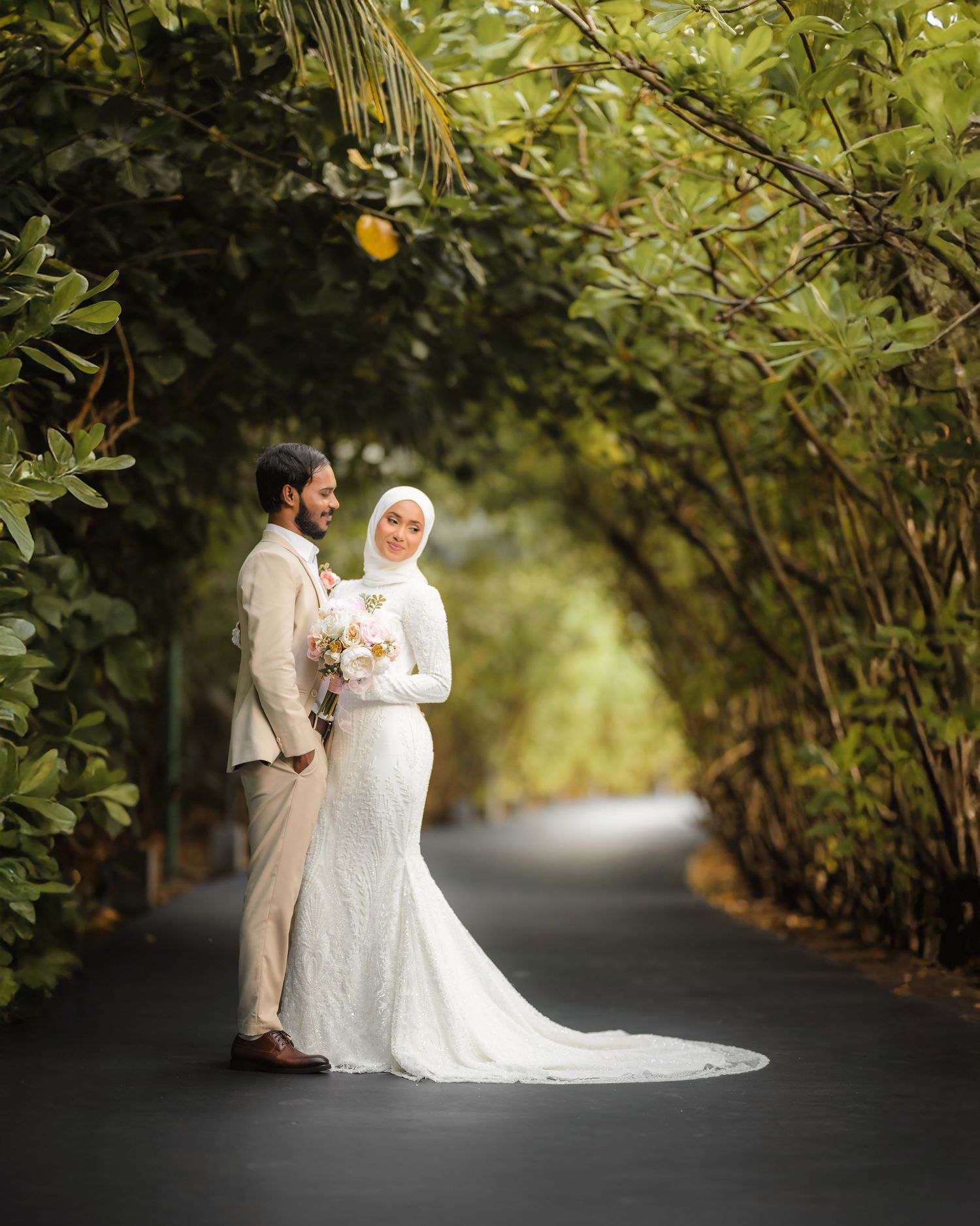 Newlyweds share an intimate moment on a lush garden path surrounded by greenery.