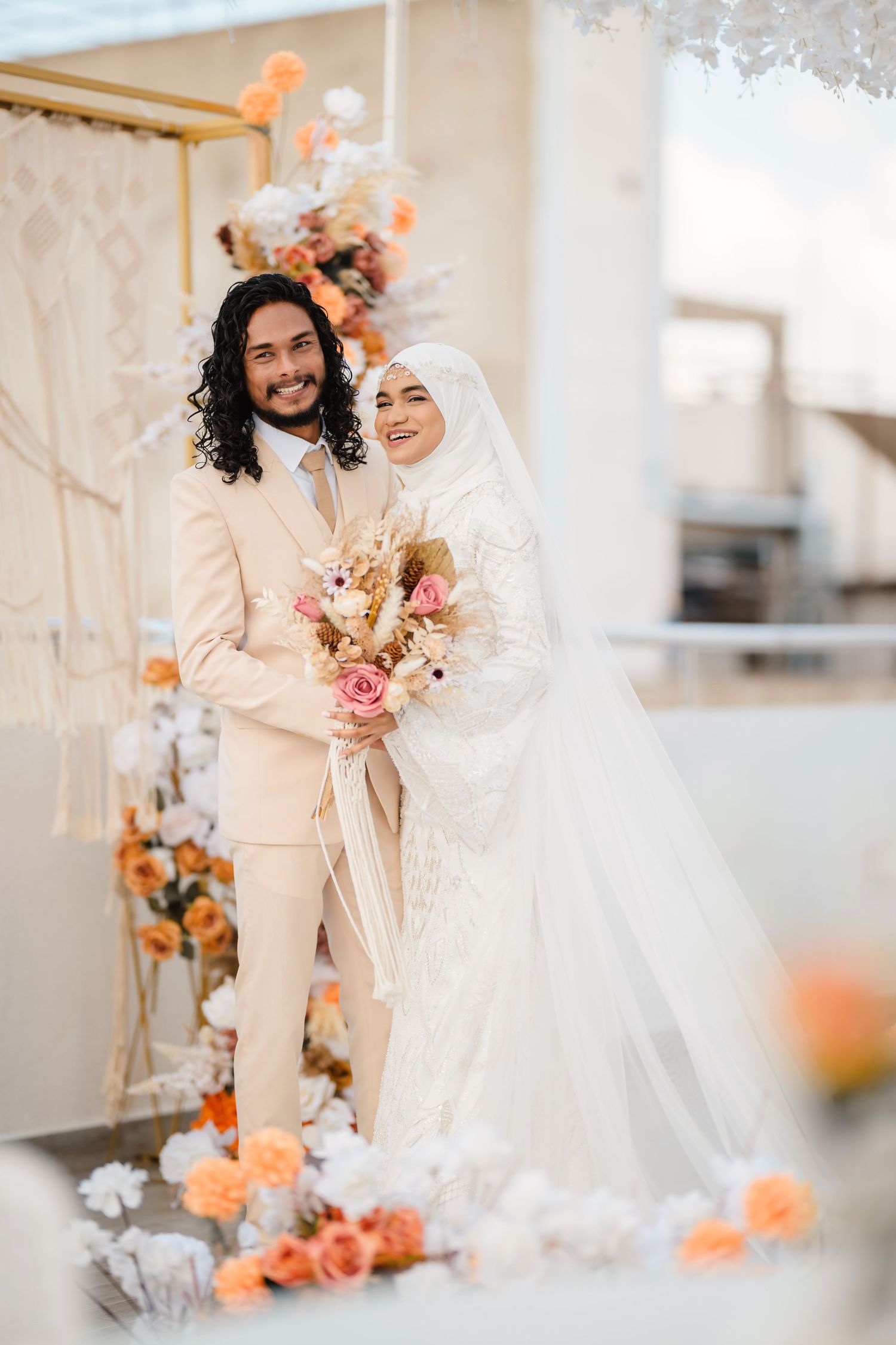 Romantic wedding portrait with couple in white and cream attire surrounded by peach-toned flowers.