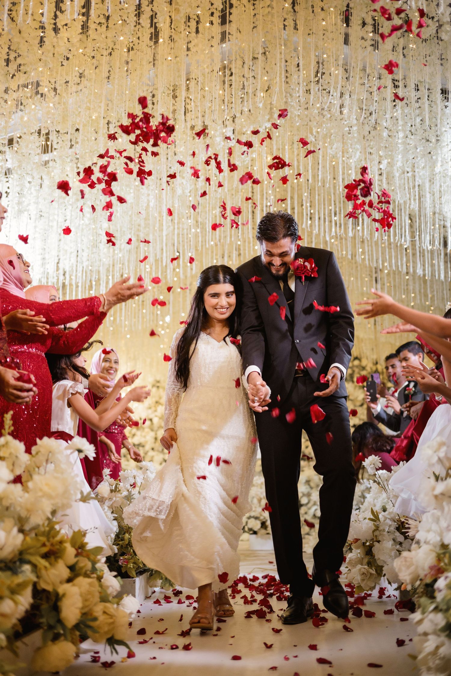Wedding celebration with red rose petals being tossed in air against crystal backdrop.