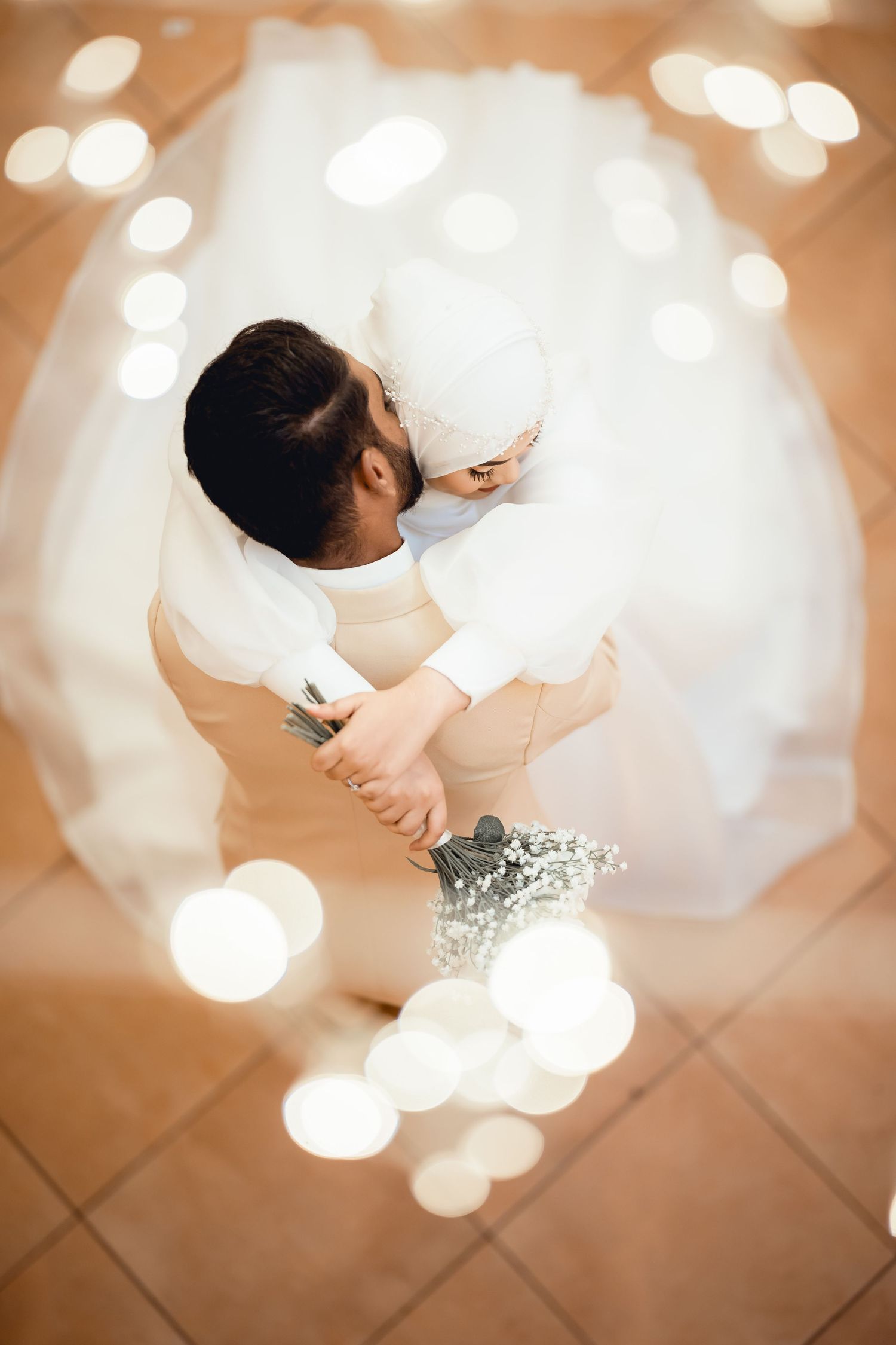 Artistic overhead shot of a wedding couple dancing on terracotta tiles with bokeh light effects.