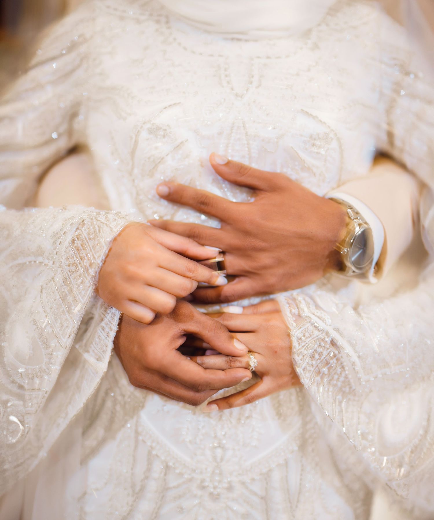 Close-up of hands displaying elegant wedding rings on white lace dress.