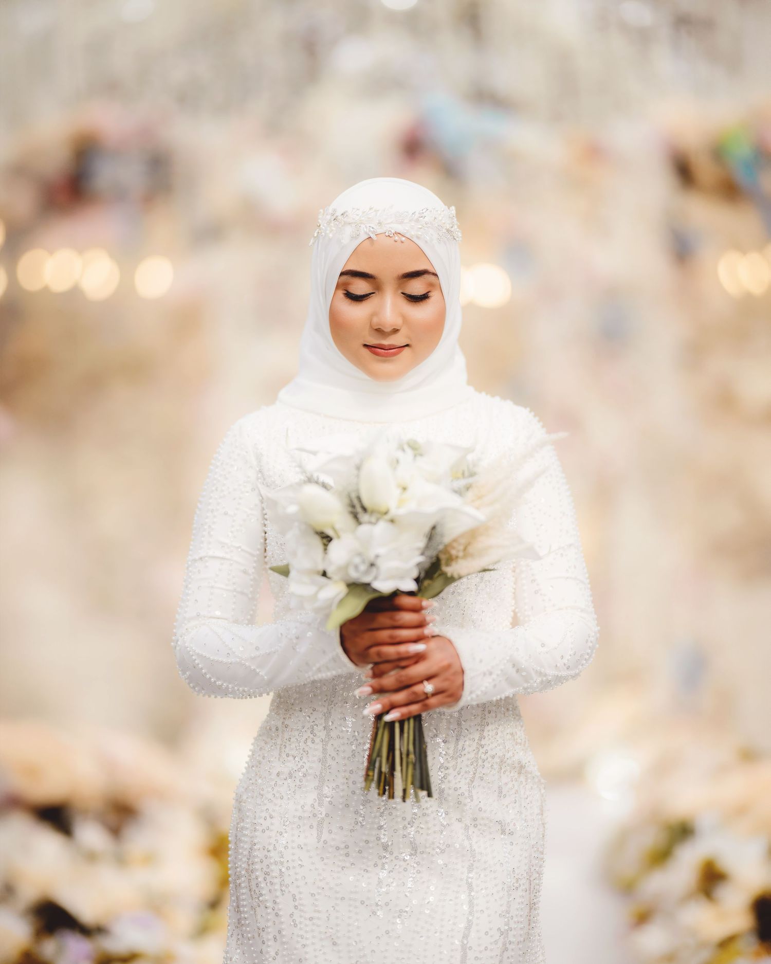 Bride in sparkling white dress admires classic white floral bouquet.