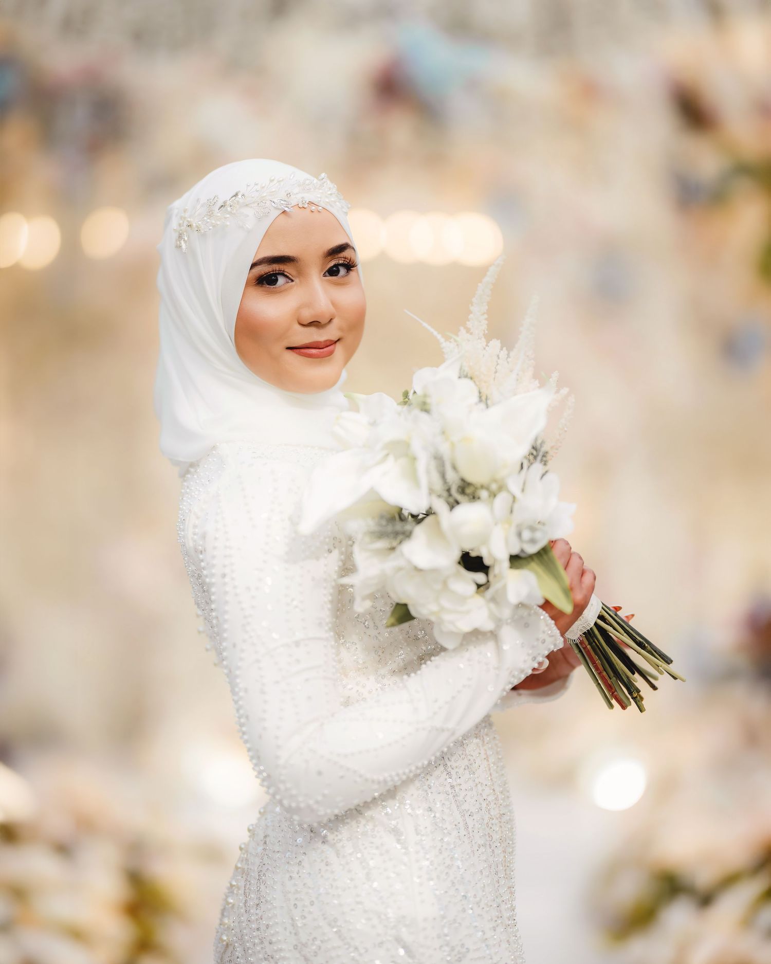 Bride in white sequined dress holds elegant bouquet of white flowers.
