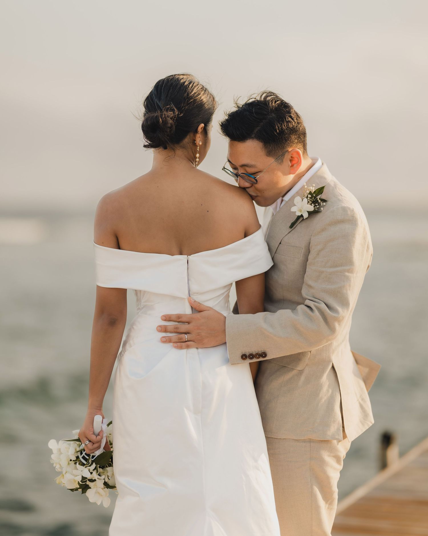Romantic wedding couple embracing in formal attire by the ocean.