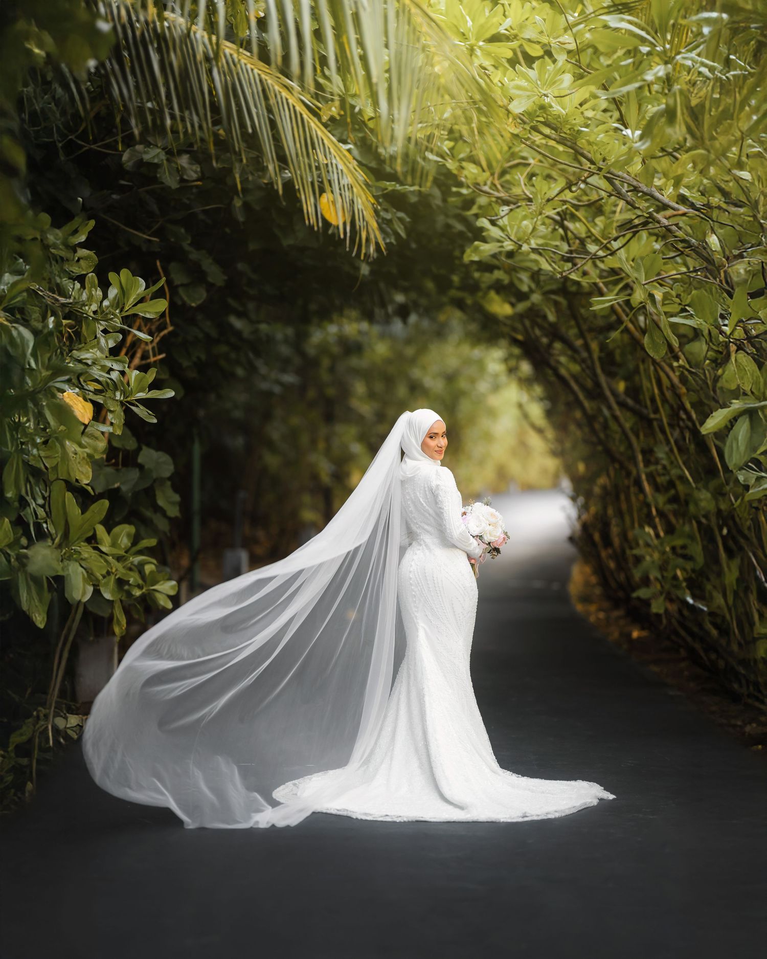 A dramatic bridal portrait with flowing veil against tropical foliage backdrop.