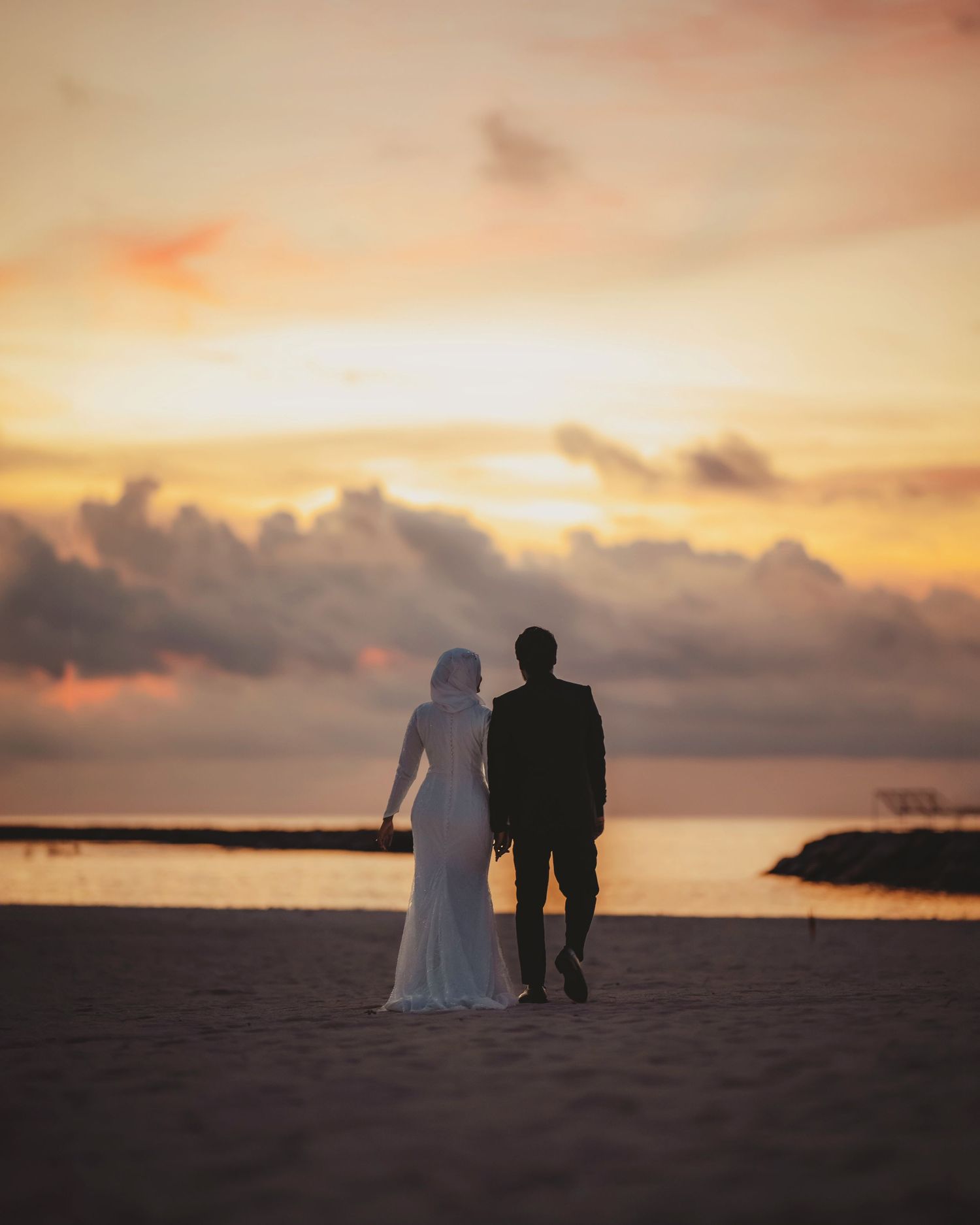 Silhouettes of a wedding couple against a dramatic orange sunset by the ocean.