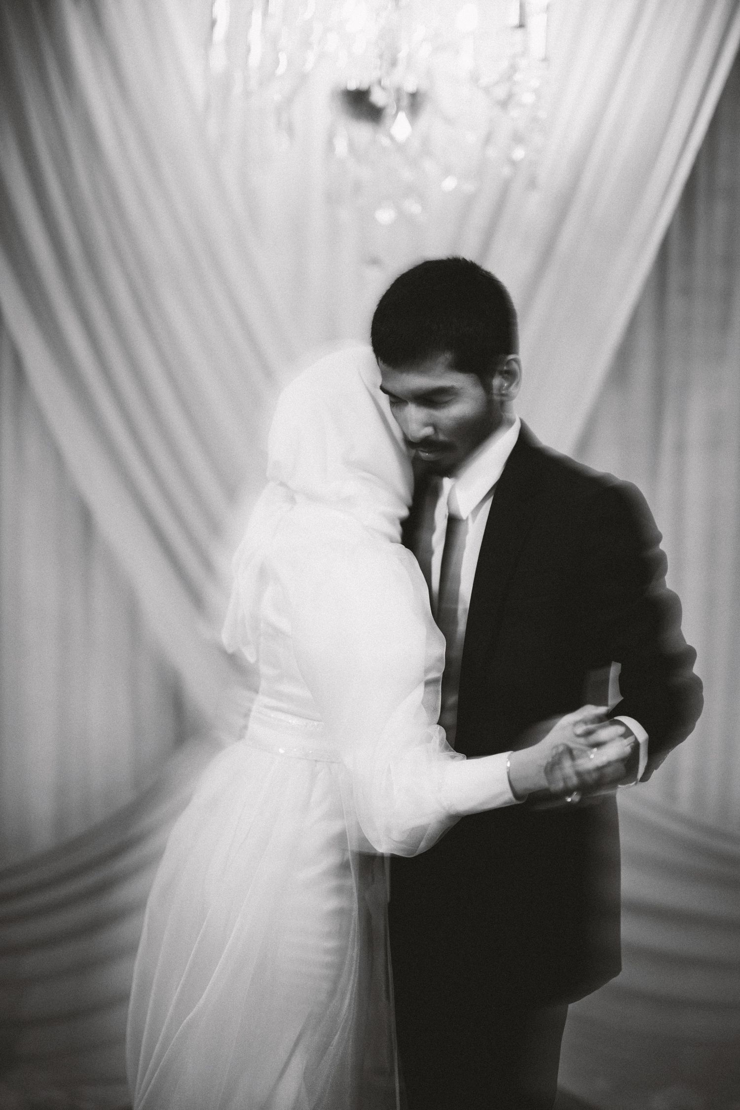 Artistic black and white sequence of newlyweds dancing in front of draped fabric backdrop.