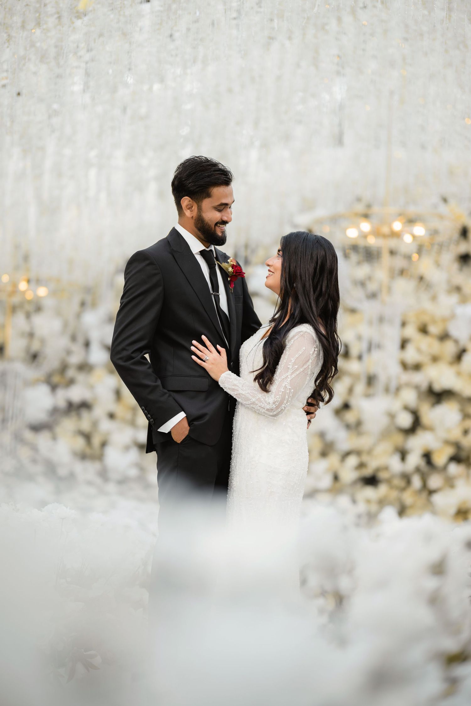 Romantic wedding portrait against white textured wall with soft lighting and floral accents.