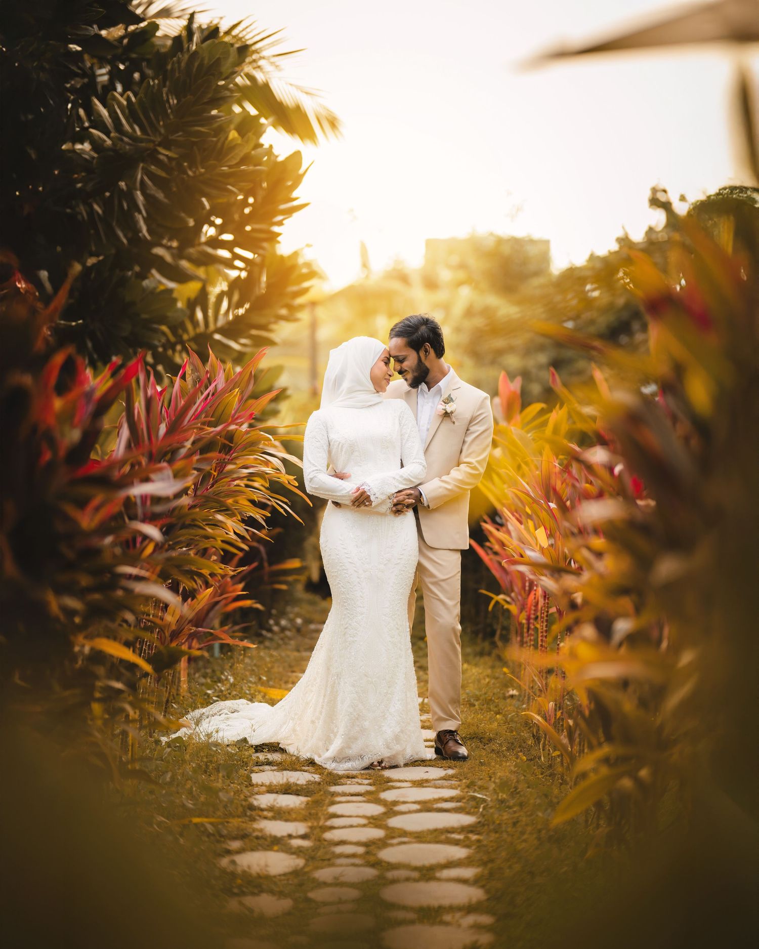 Wedding couple poses at sunset among tropical foliage with warm golden light.