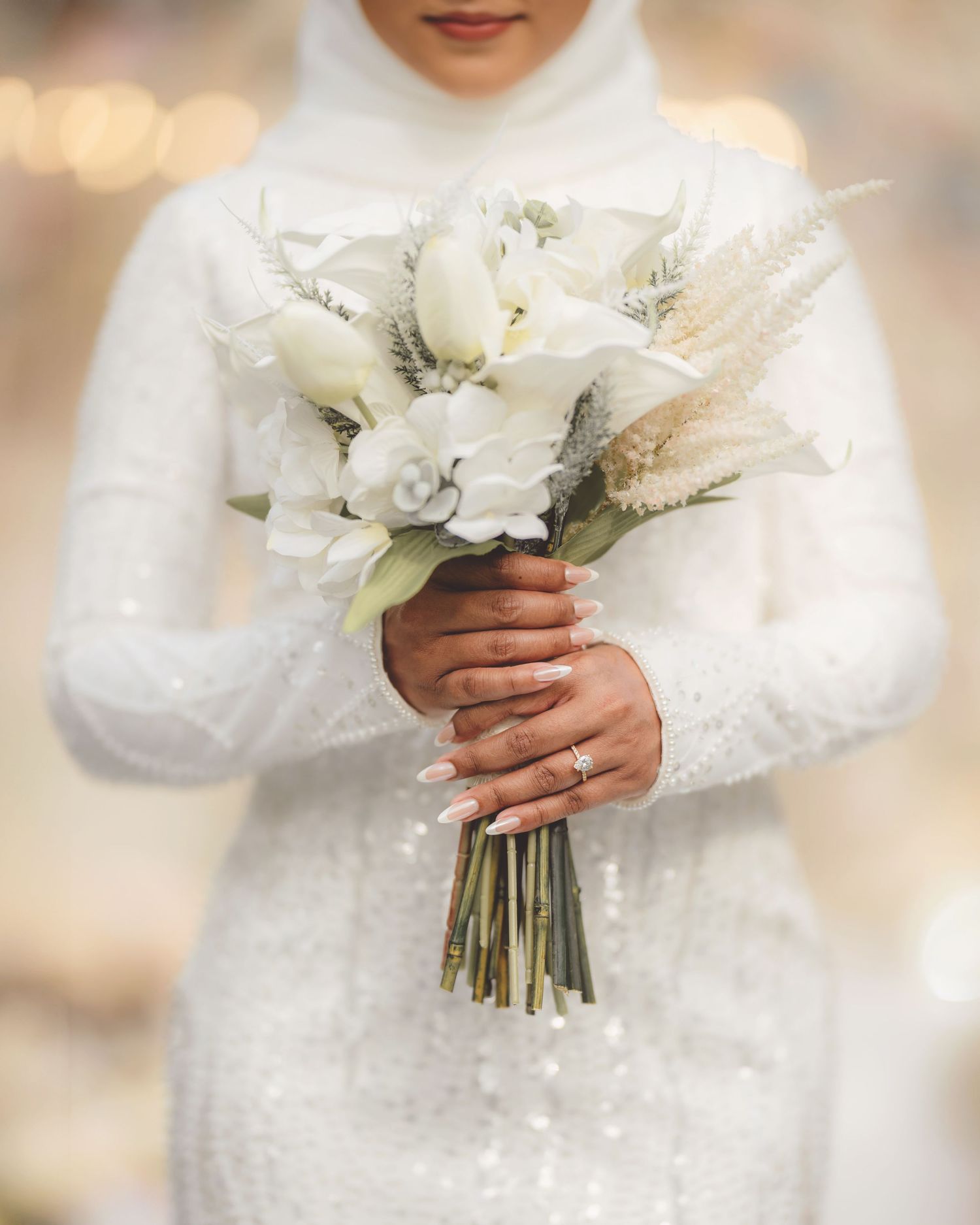 Close-up of white bridal bouquet with lilies and roses held against lace dress.