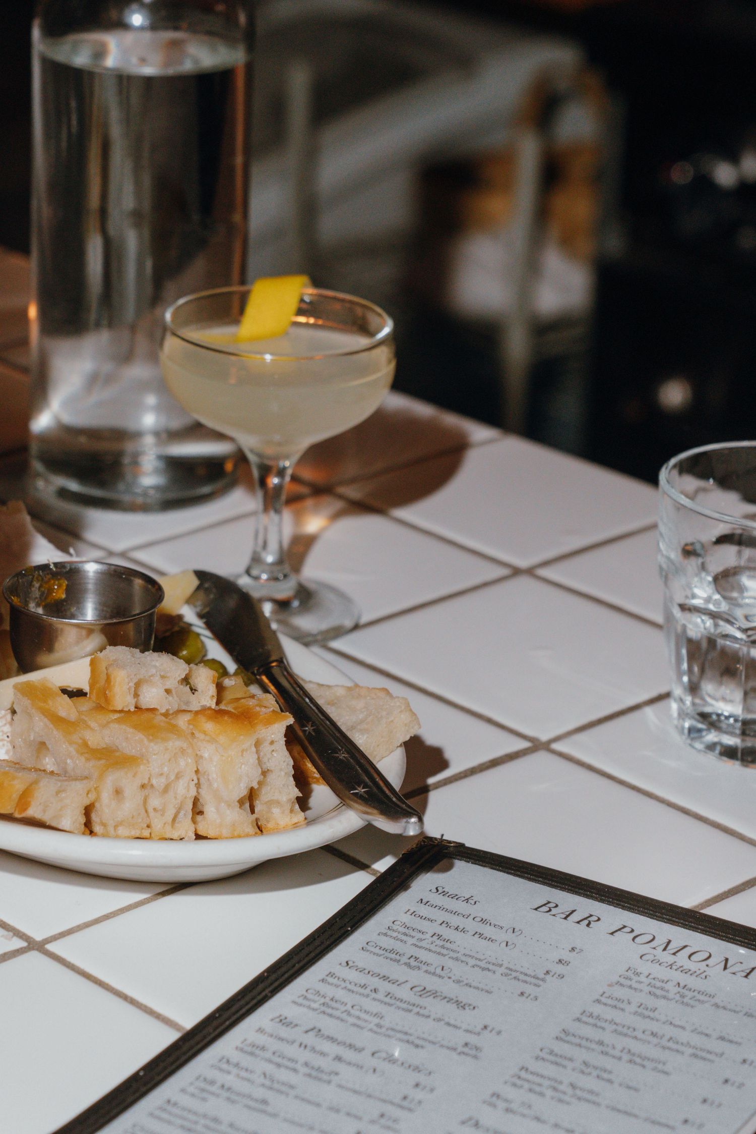 Cocktail and bread service at Bar Pomona restaurant with white tiled table.