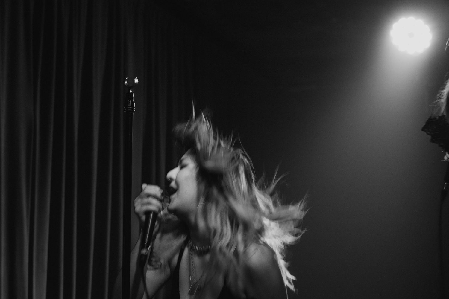 Black and white photo of female vocalist singing passionately with hair flying on stage.