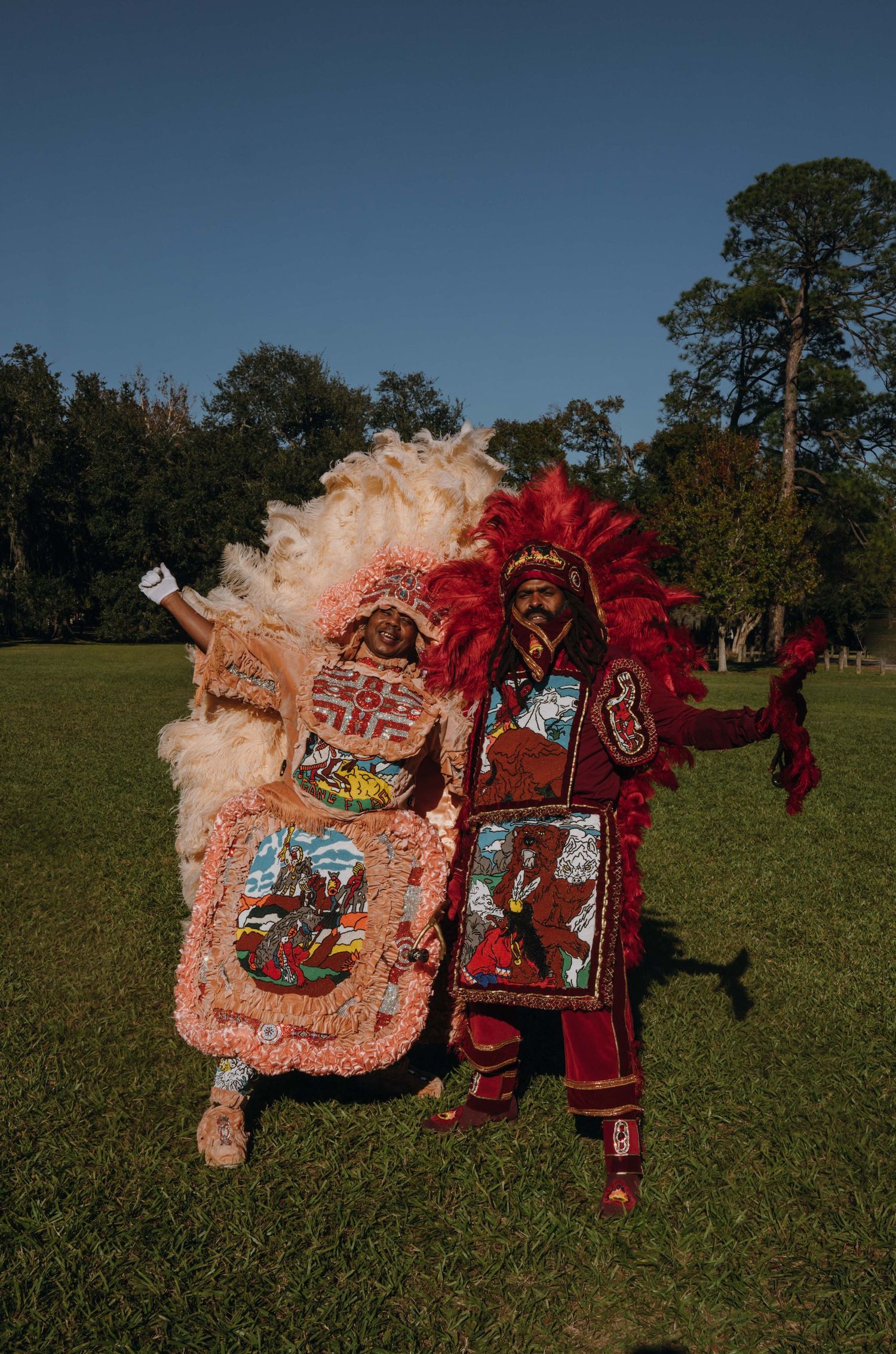 Two New Orleans Mardi Gras Indians display intricate beaded patchwork suits with colorful feathered headdresses outdoors.
