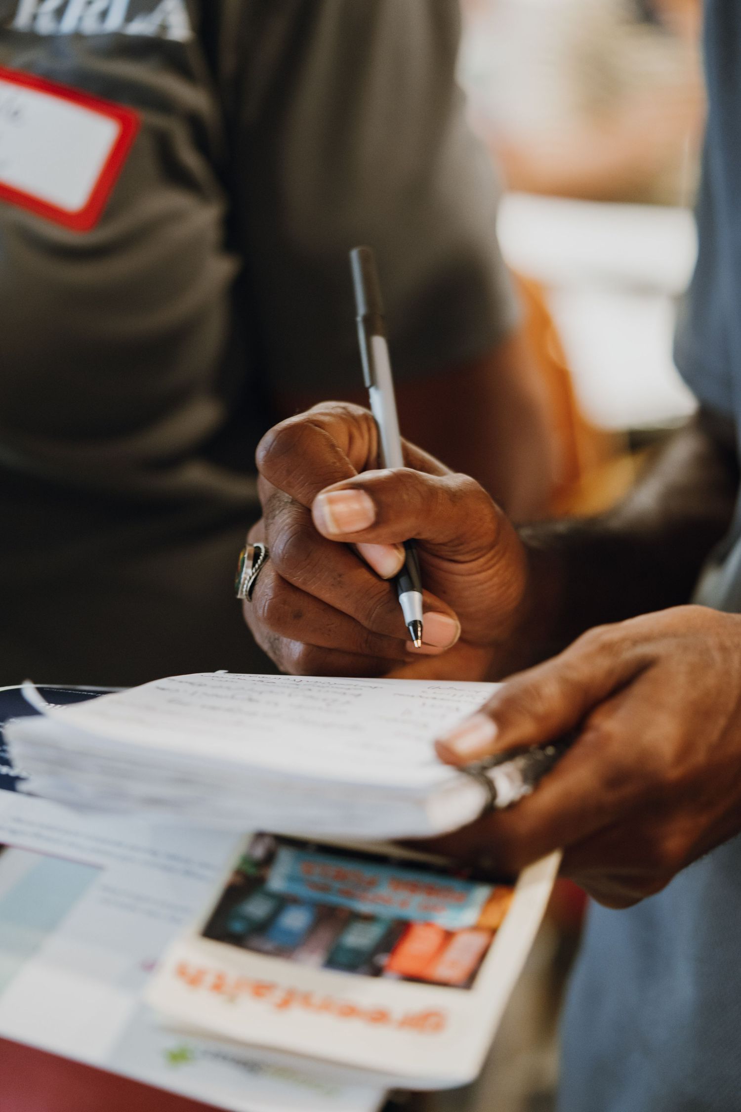 Close-up of hands signing documents with pen at community registration table.