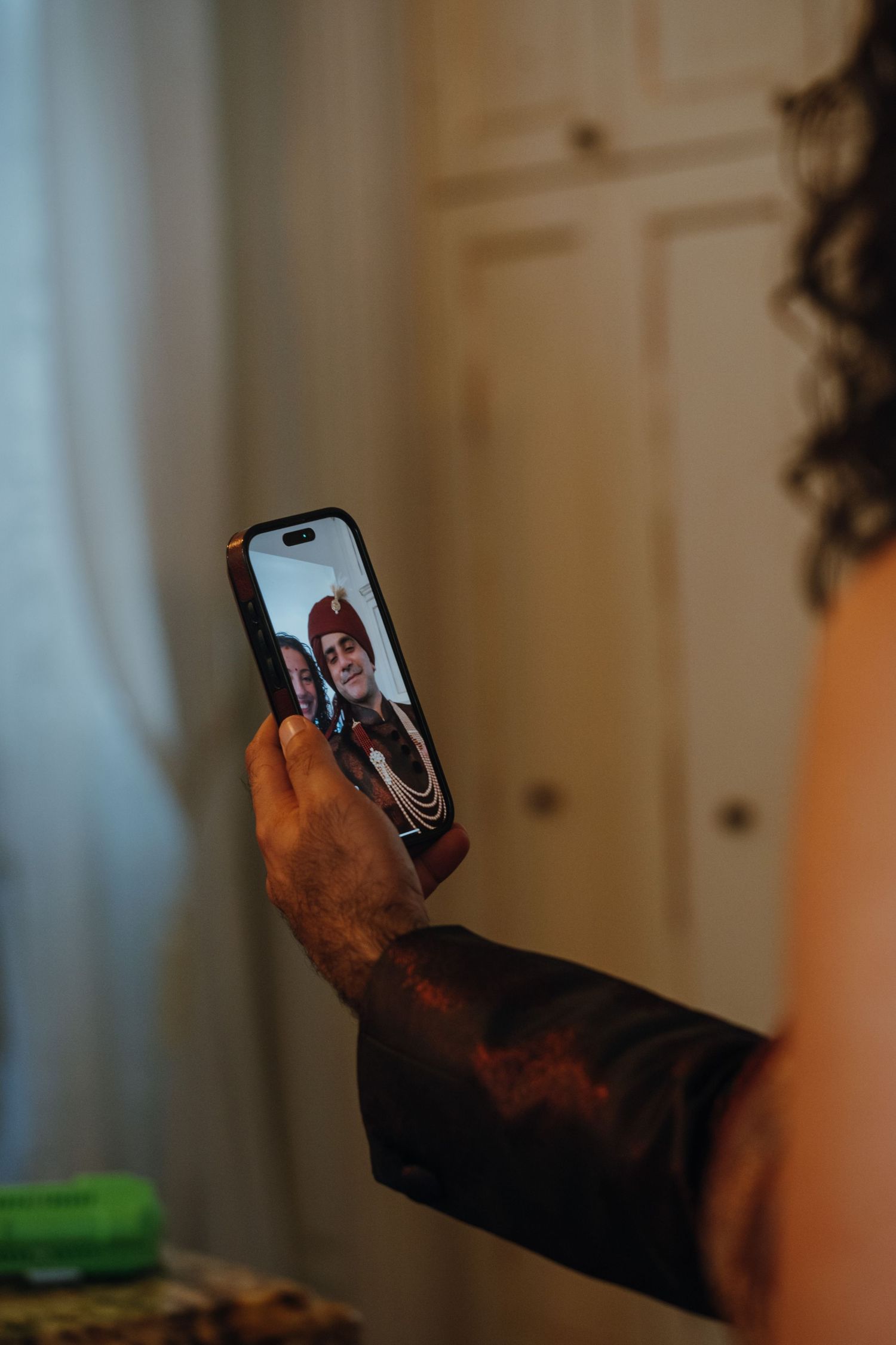 Groom in traditional red turban captured on smartphone screen during wedding video call.