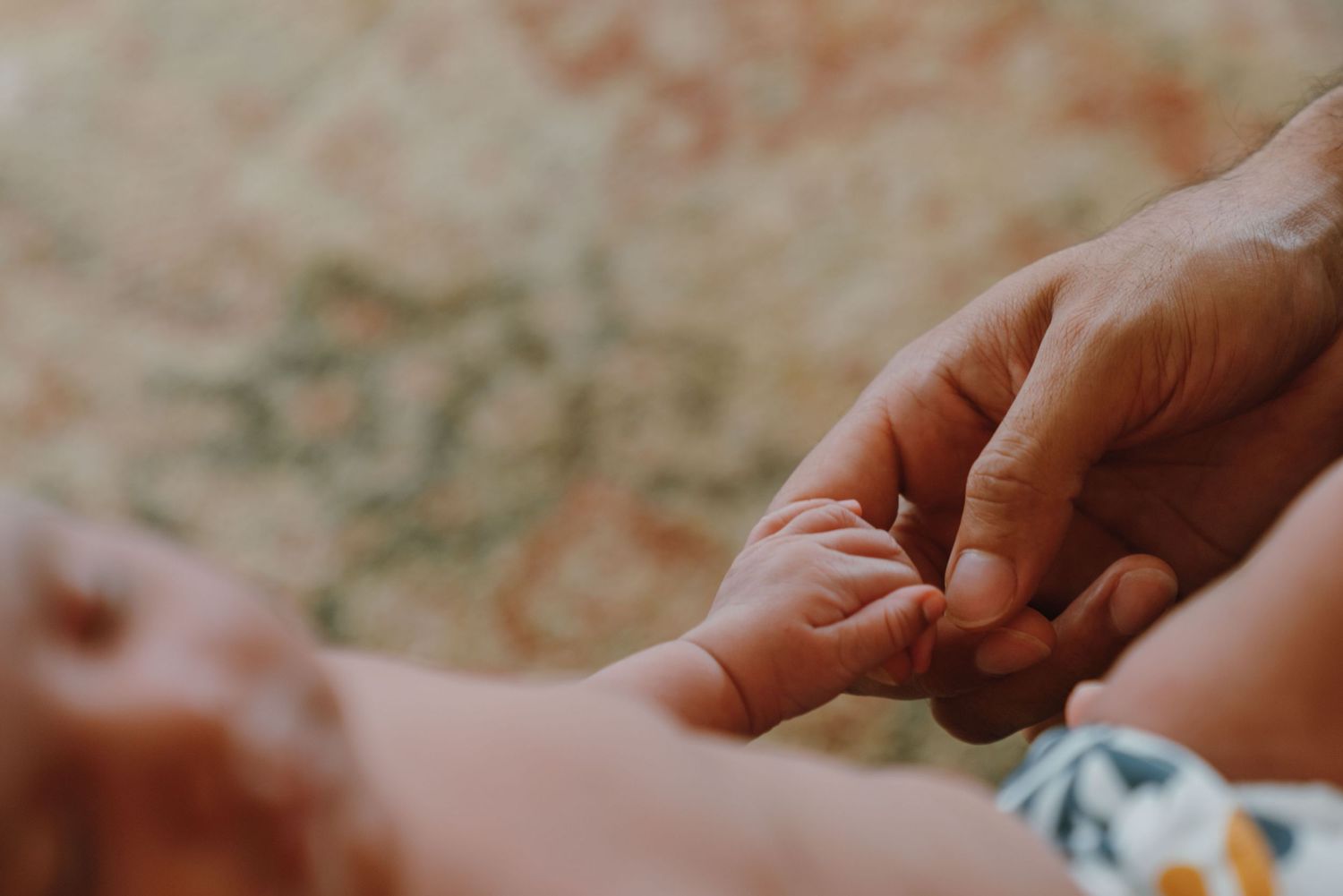 Close-up of newborn baby grasping adult finger on soft patterned background. New Orleans, Louisiana, Mississippi