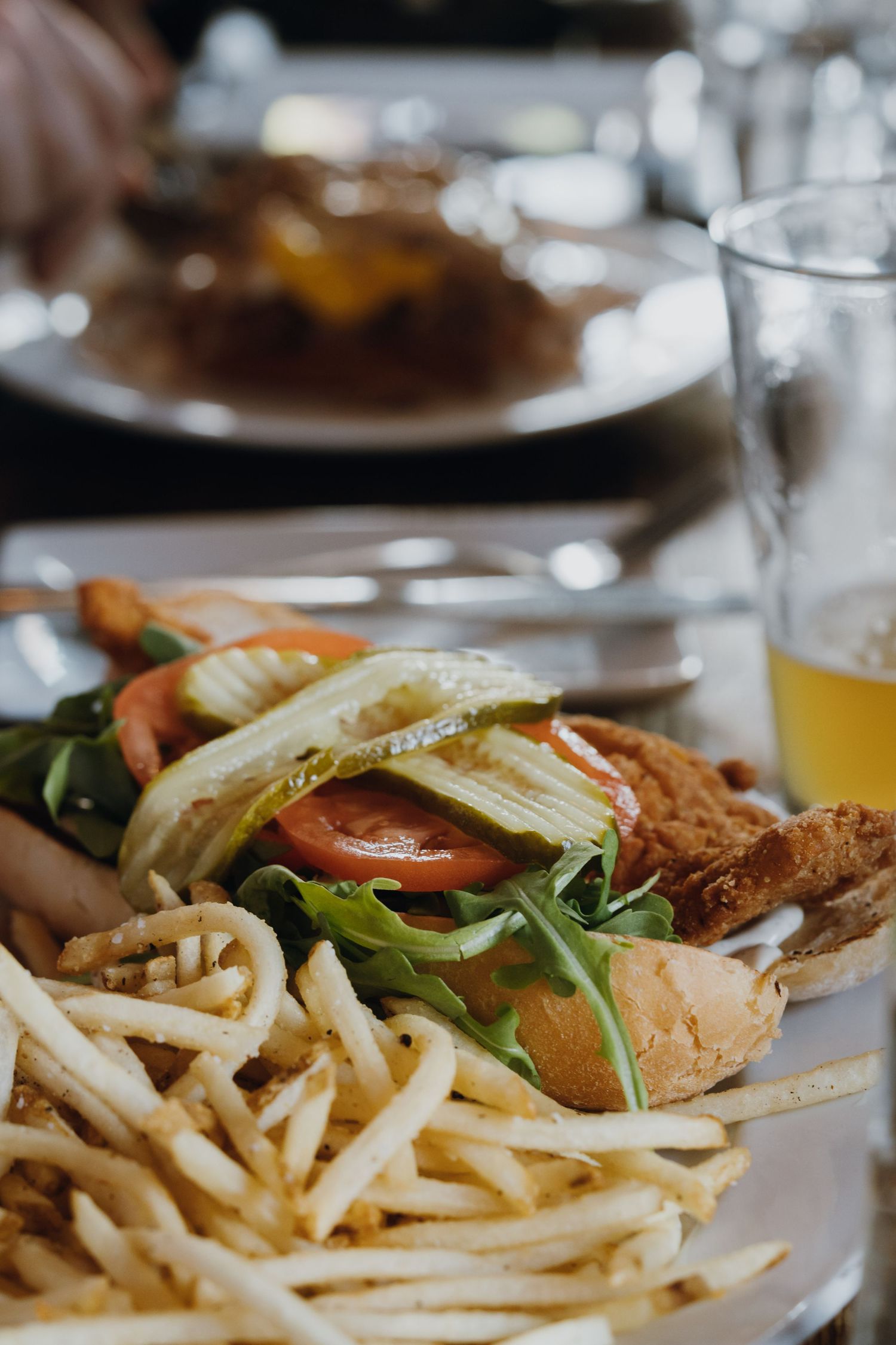 Gourmet burger with fresh tomatoes, arugula, and pickles served with crispy french fries on a plate.