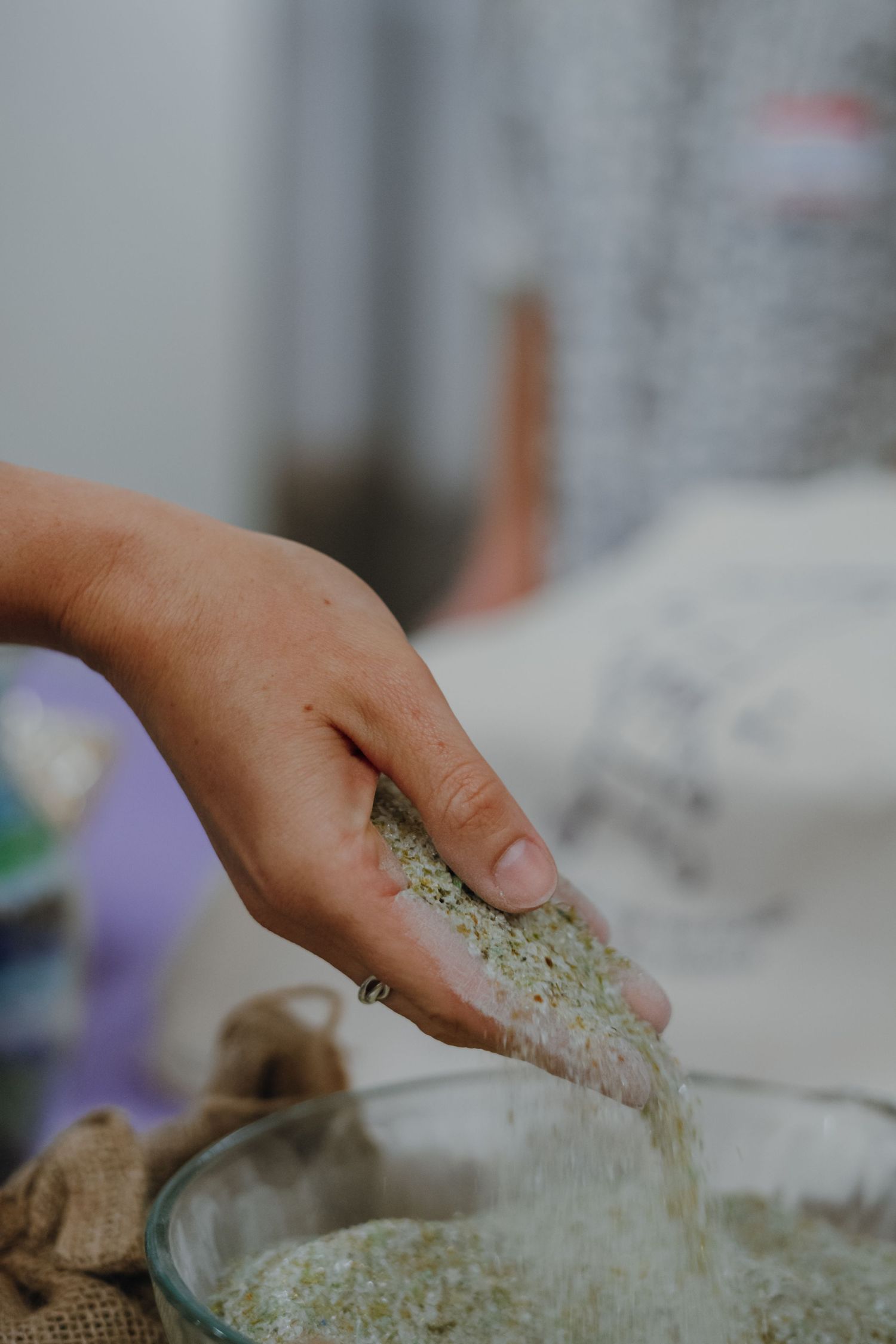 Hand sifting green herb powder into a glass bowl at a natural materials workshop.