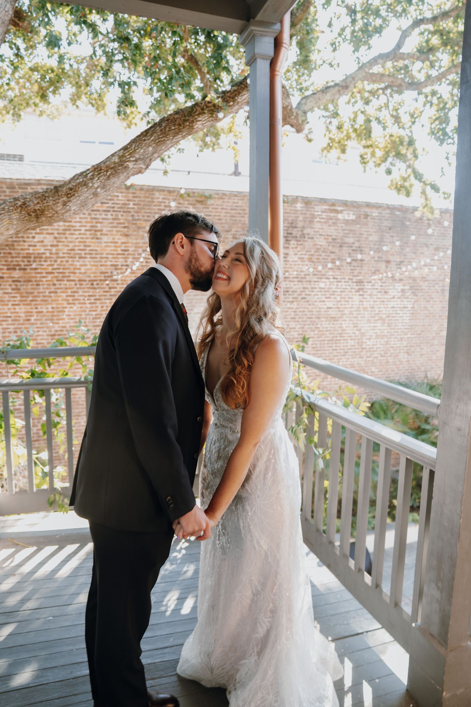 Bride and groom sharing tender kiss on wooden porch under oak tree at wedding.