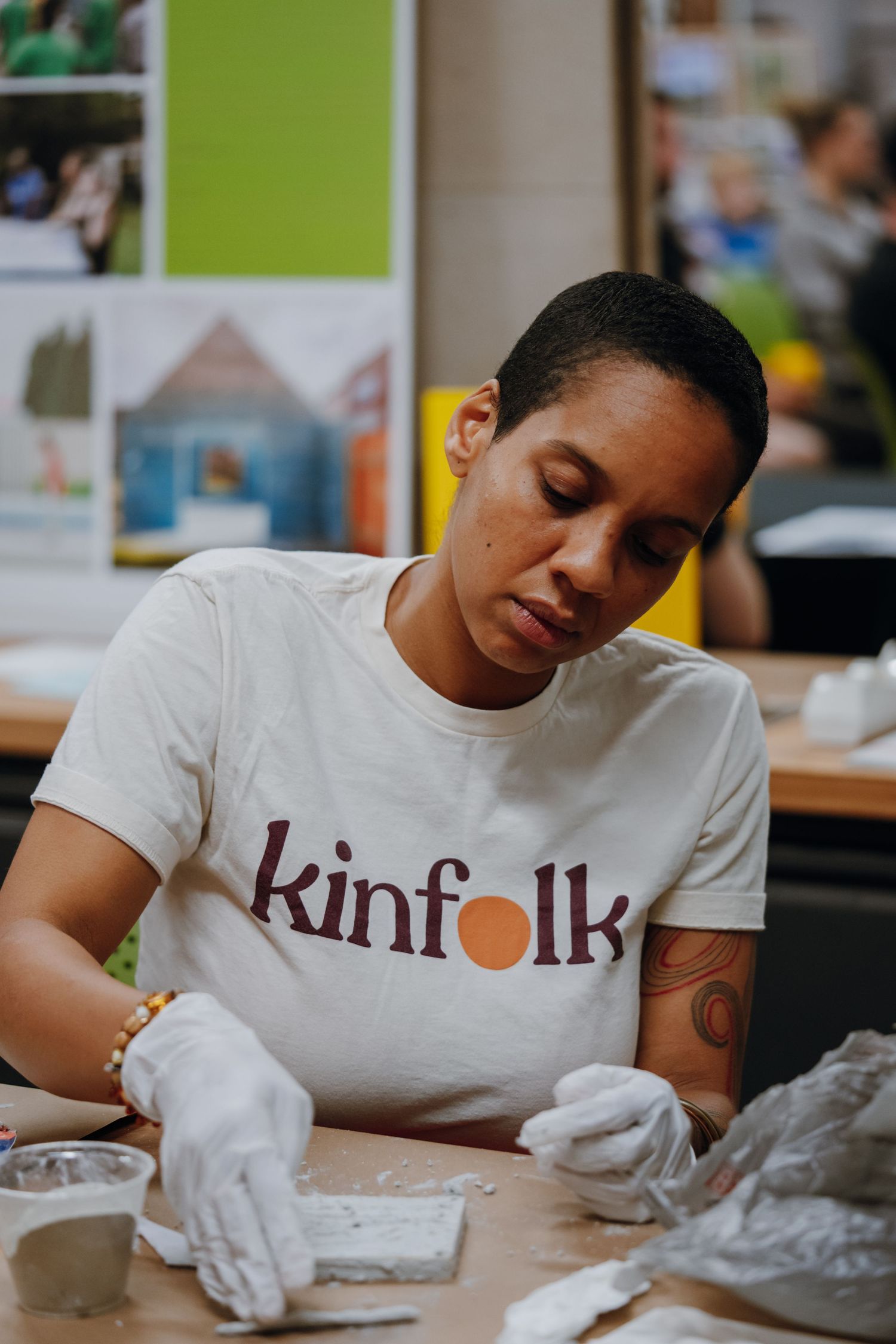 Woman in Kinfolk t-shirt wearing white gloves works with clay at a table in an art studio.