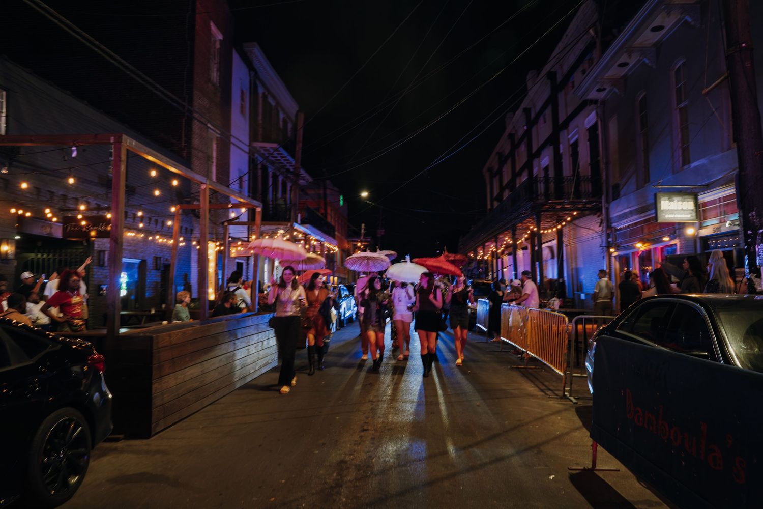 A lively nighttime street scene with string lights, colorful umbrellas, and crowds of people socializing outdoors.