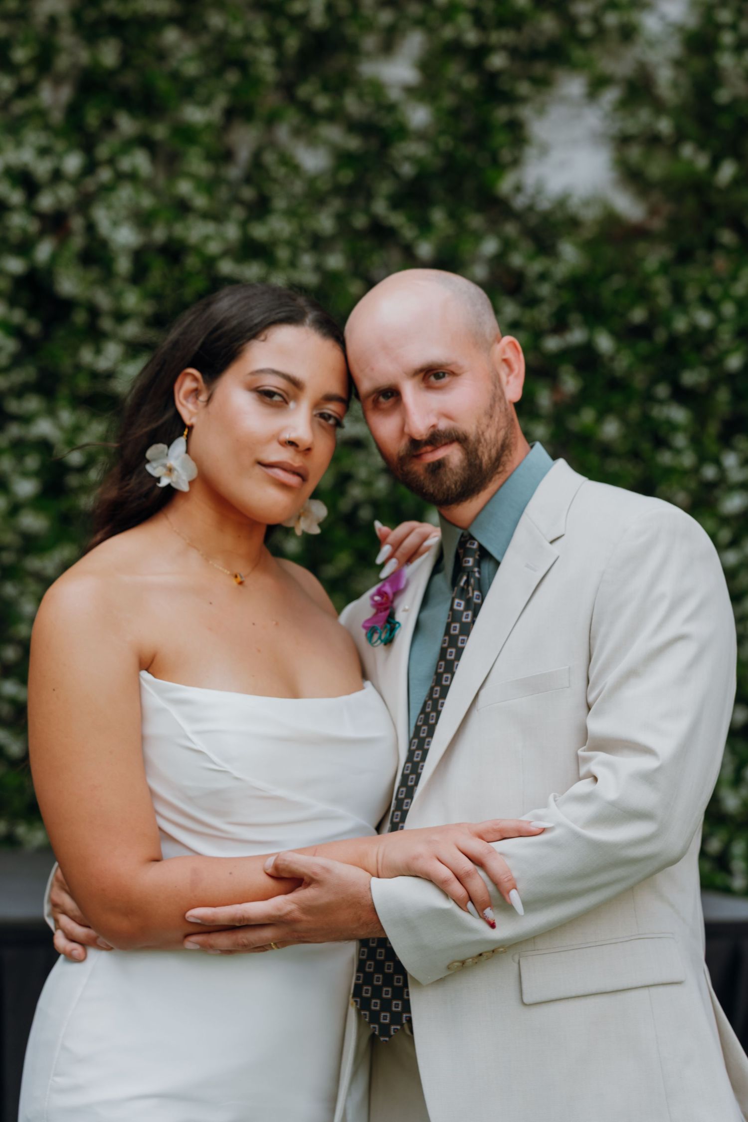 Bride and groom pose intimately together in front of lush green ivy wall at wedding.