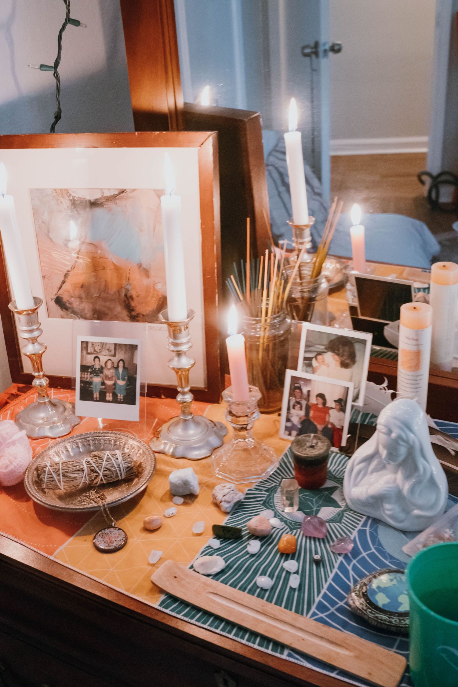 Spiritual altar with candles, crystals, sage, Polaroid photos and artwork on wooden table.