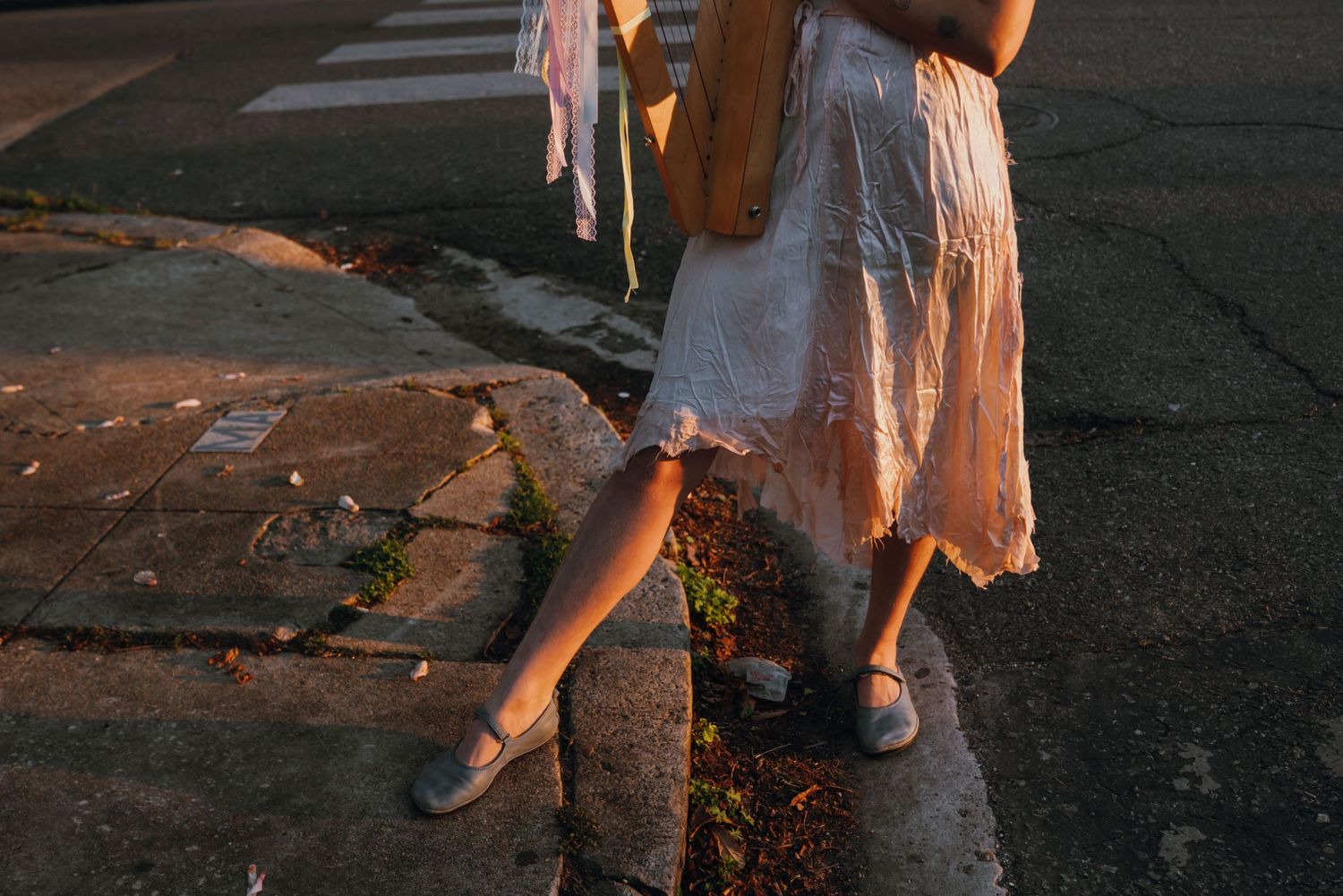 Woman in white lace dress and mary jane shoes standing on urban sidewalk at golden hour.