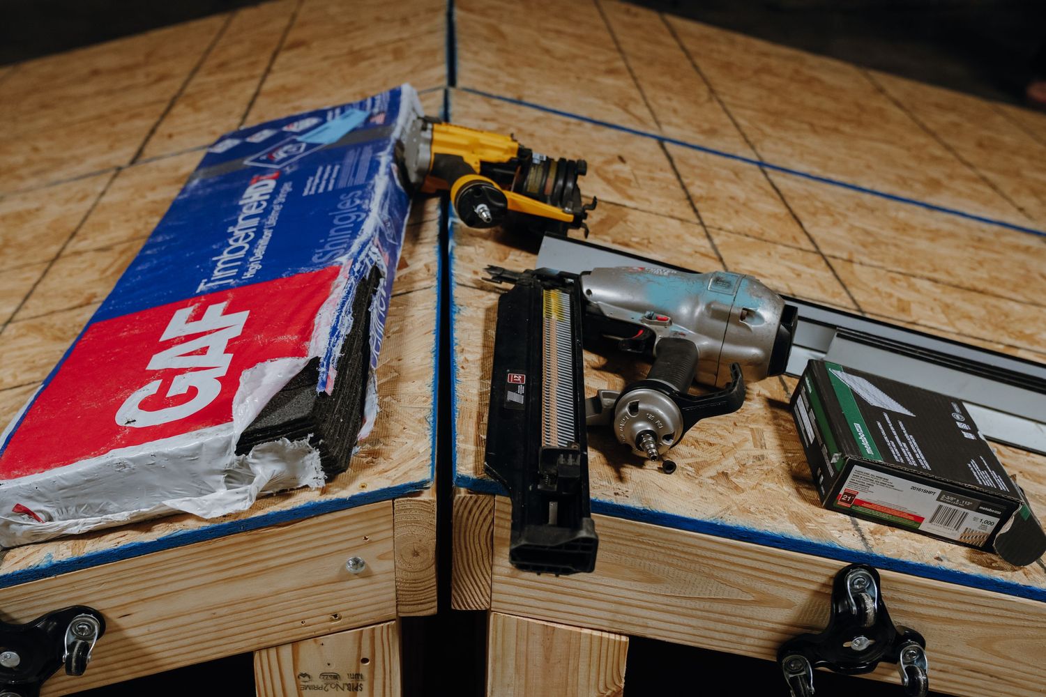 Roofing tools and GAF materials laid out on a wooden surface at a construction site.