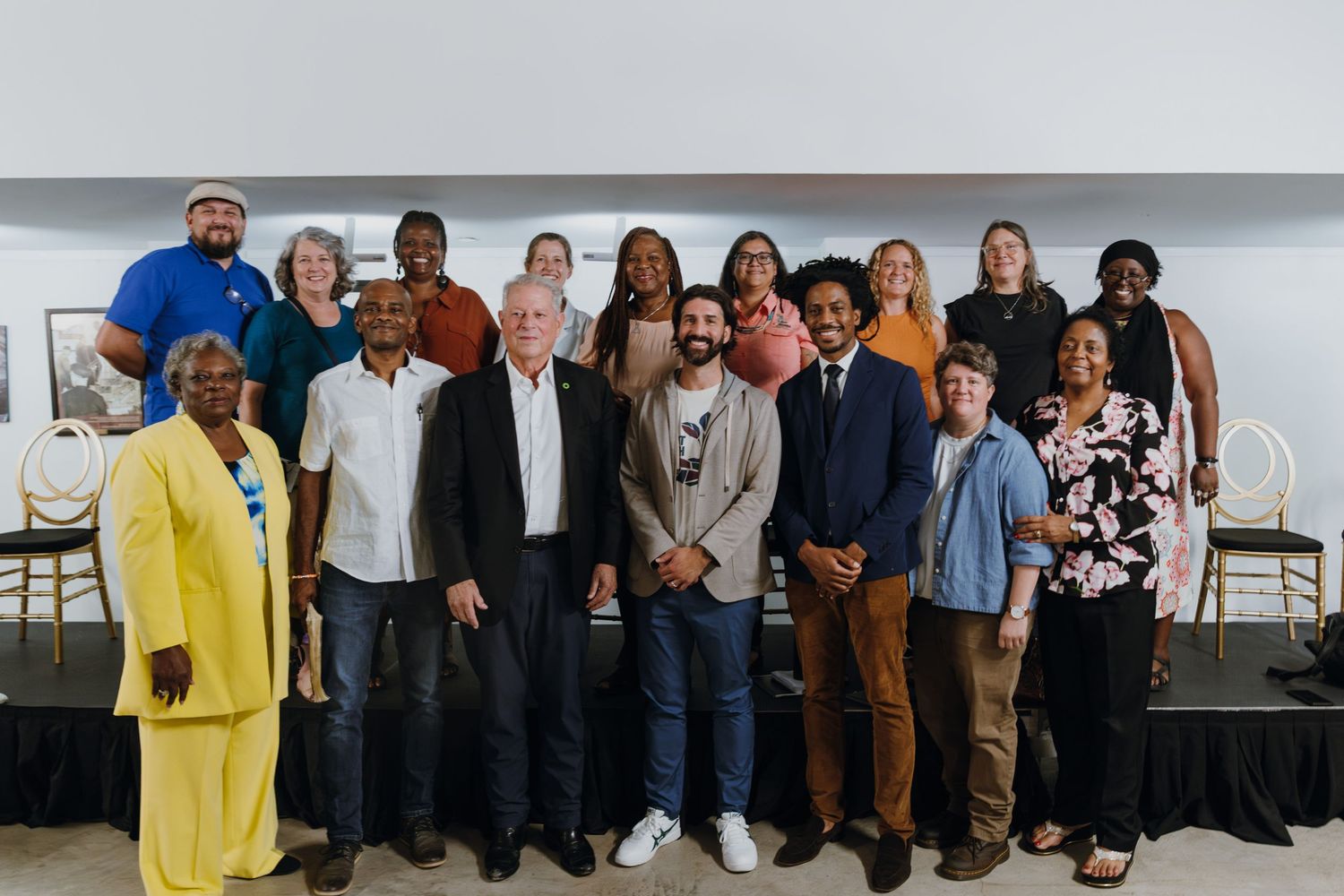 A diverse group of approximately fifteen people pose together for a group photo at an indoor event.