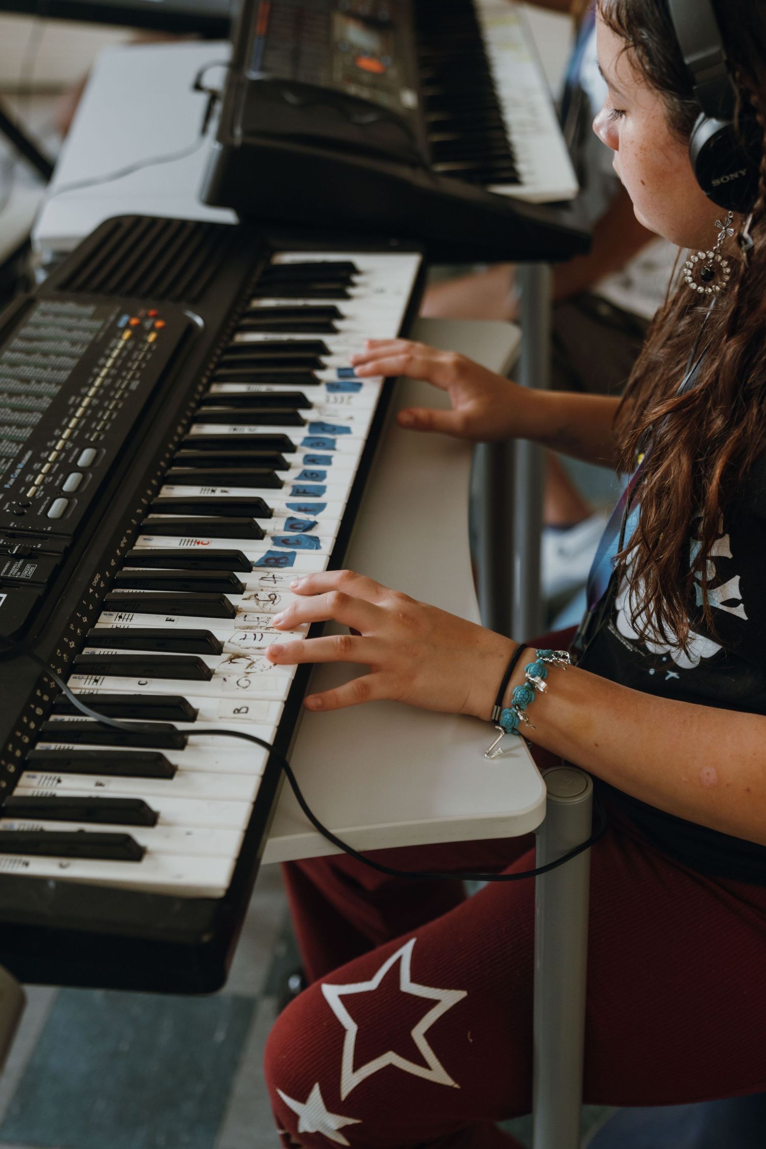Teen girl with headphones plays keyboard piano in music class, wearing star-print pants and bracelet. New Orleans, Louisiana, Mississippi