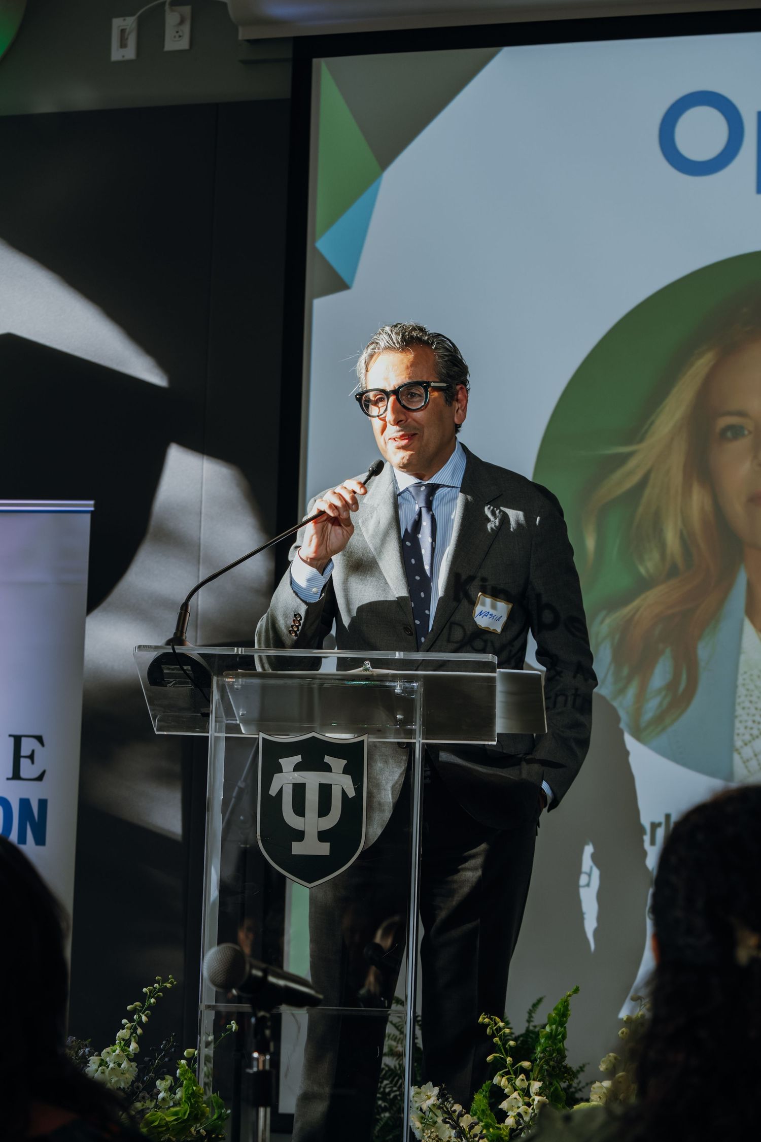 Man in suit speaking at a podium during a Tulane University formal presentation event.