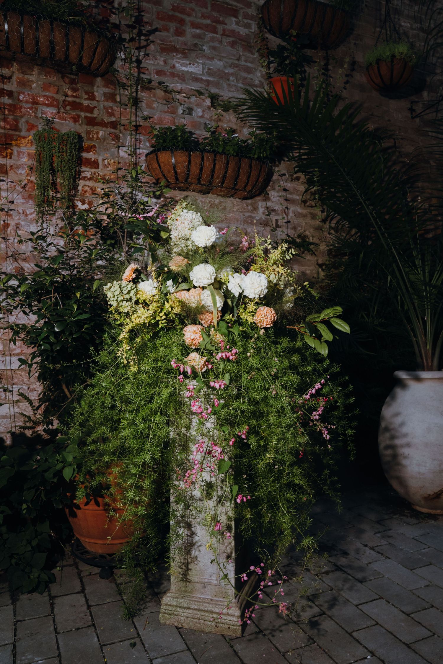Elegant floral arrangement of white and peach blooms on stone pedestal against rustic brick wall backdrop. New Orleans, Louisiana, Mississip