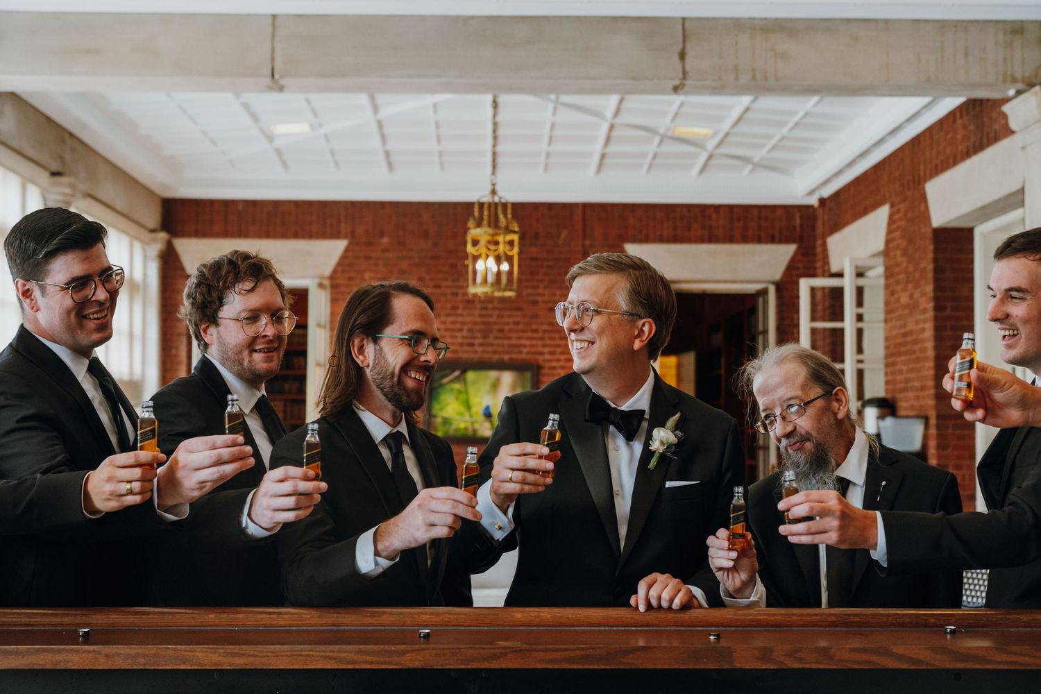 Groom and groomsmen in black tuxedos toasting with drinks at a wooden bar. New Orleans, Louisiana, Mississippi