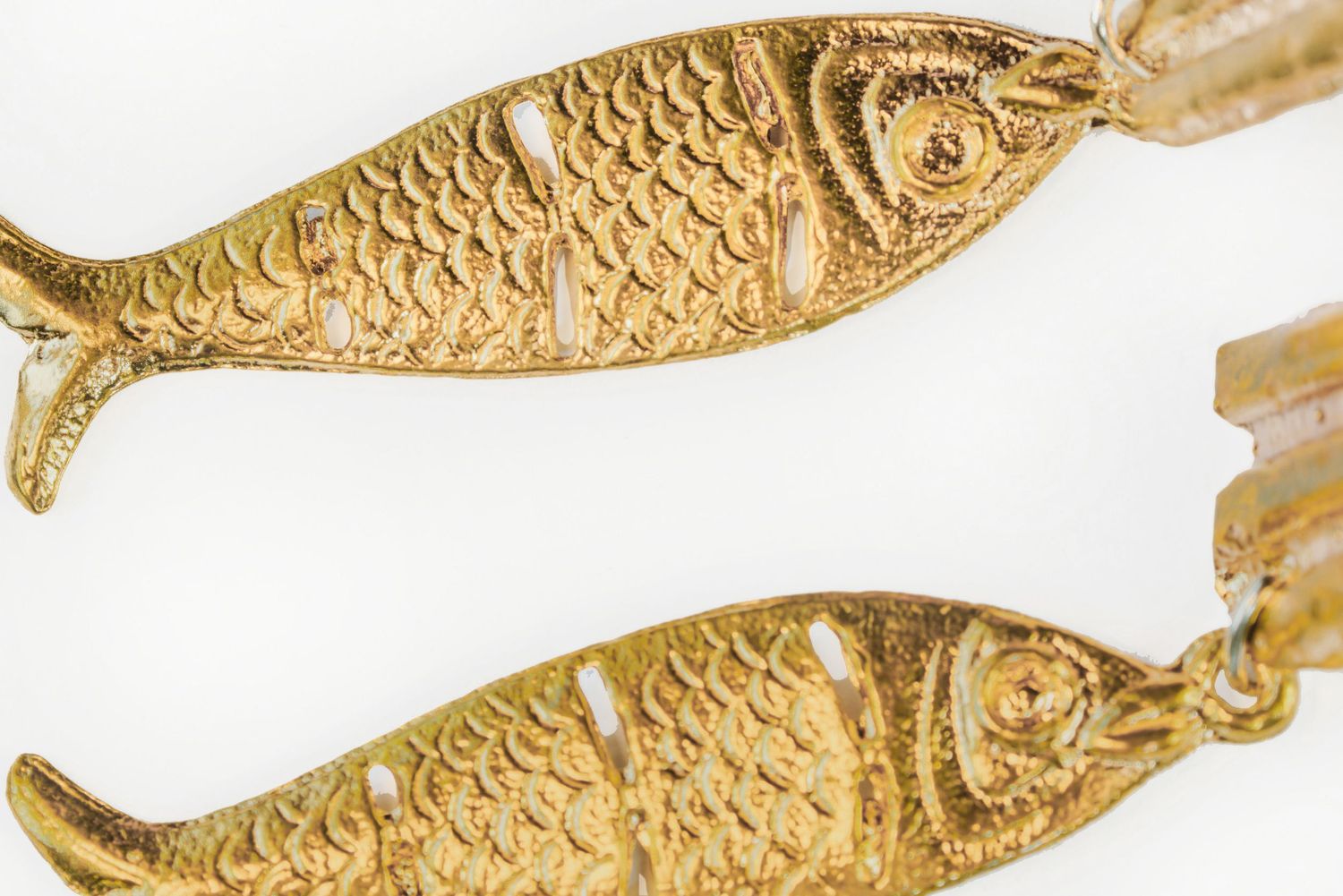 Pair of detailed gold fish-shaped jewelry pieces with scale texture on white background.