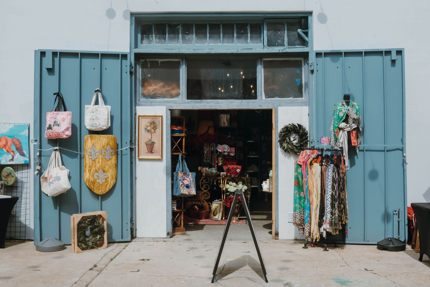 Colorful boutique shop with blue barn doors displaying bags, artwork, and clothing outside.
