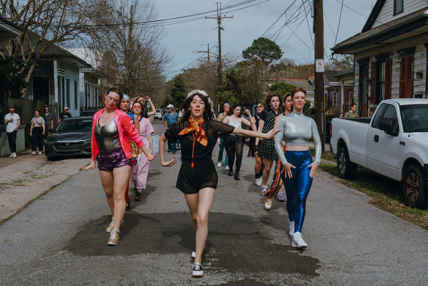 Women in vibrant outfits dancing and marching down a residential street.