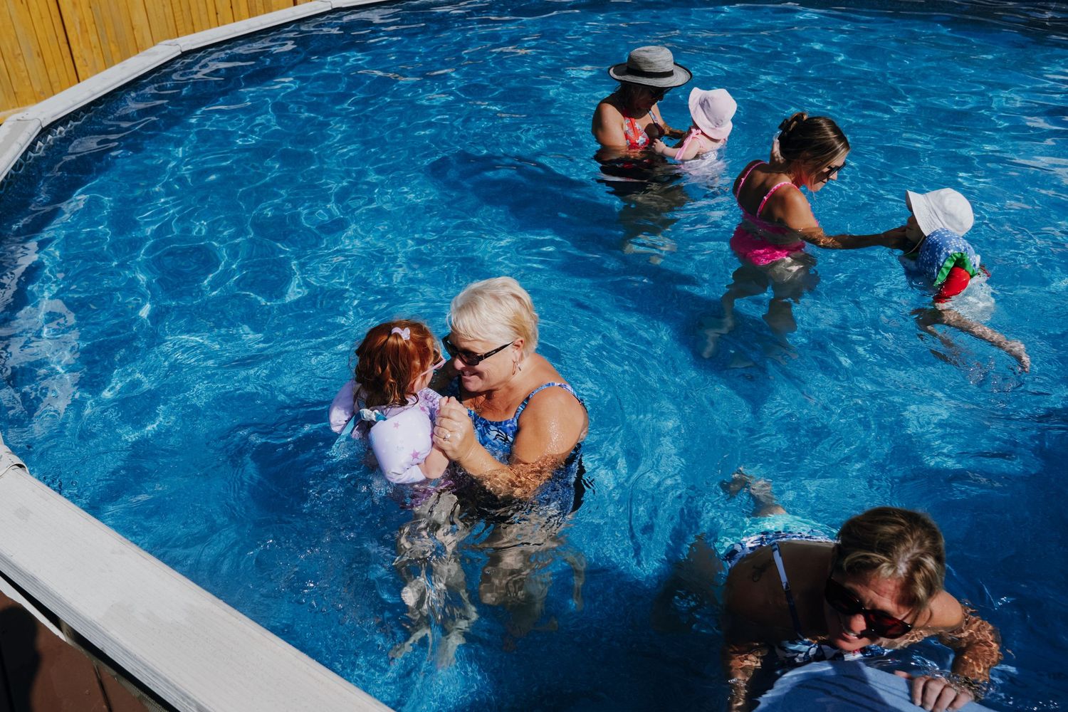 Family enjoying a summer day together in a backyard swimming pool with children.
