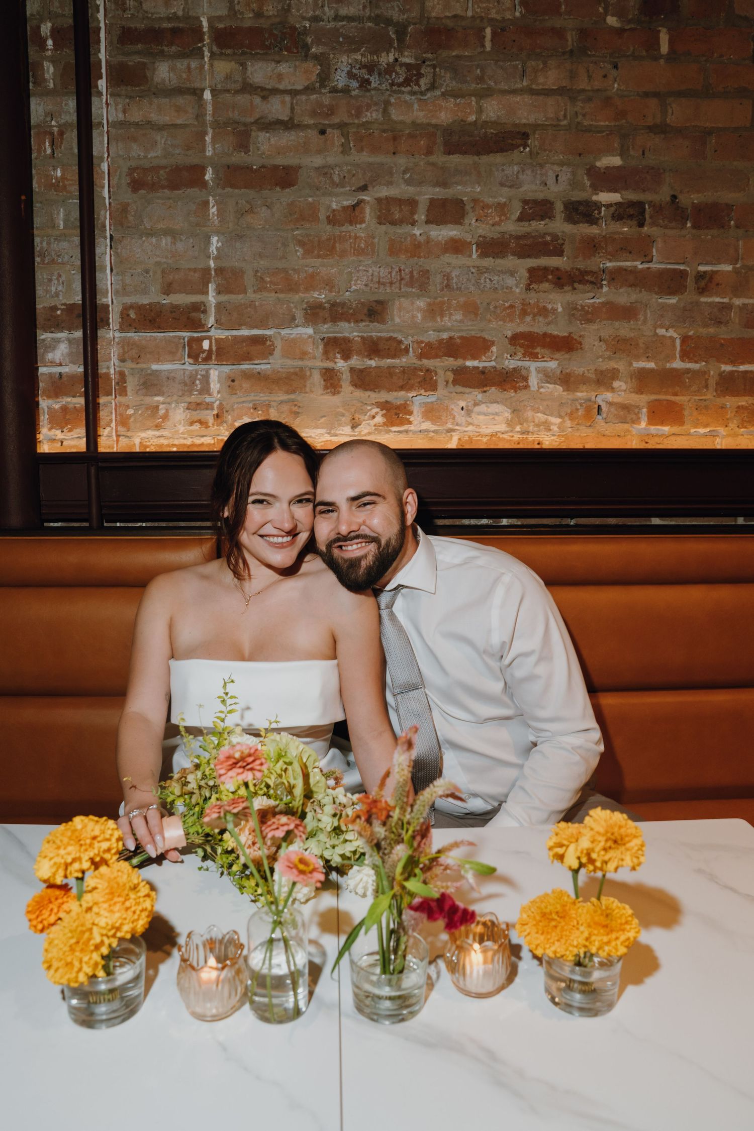 Happy bride and groom sit together at reception table adorned with colorful yellow and orange floral centerpieces. New Orleans, Louisiana, M
