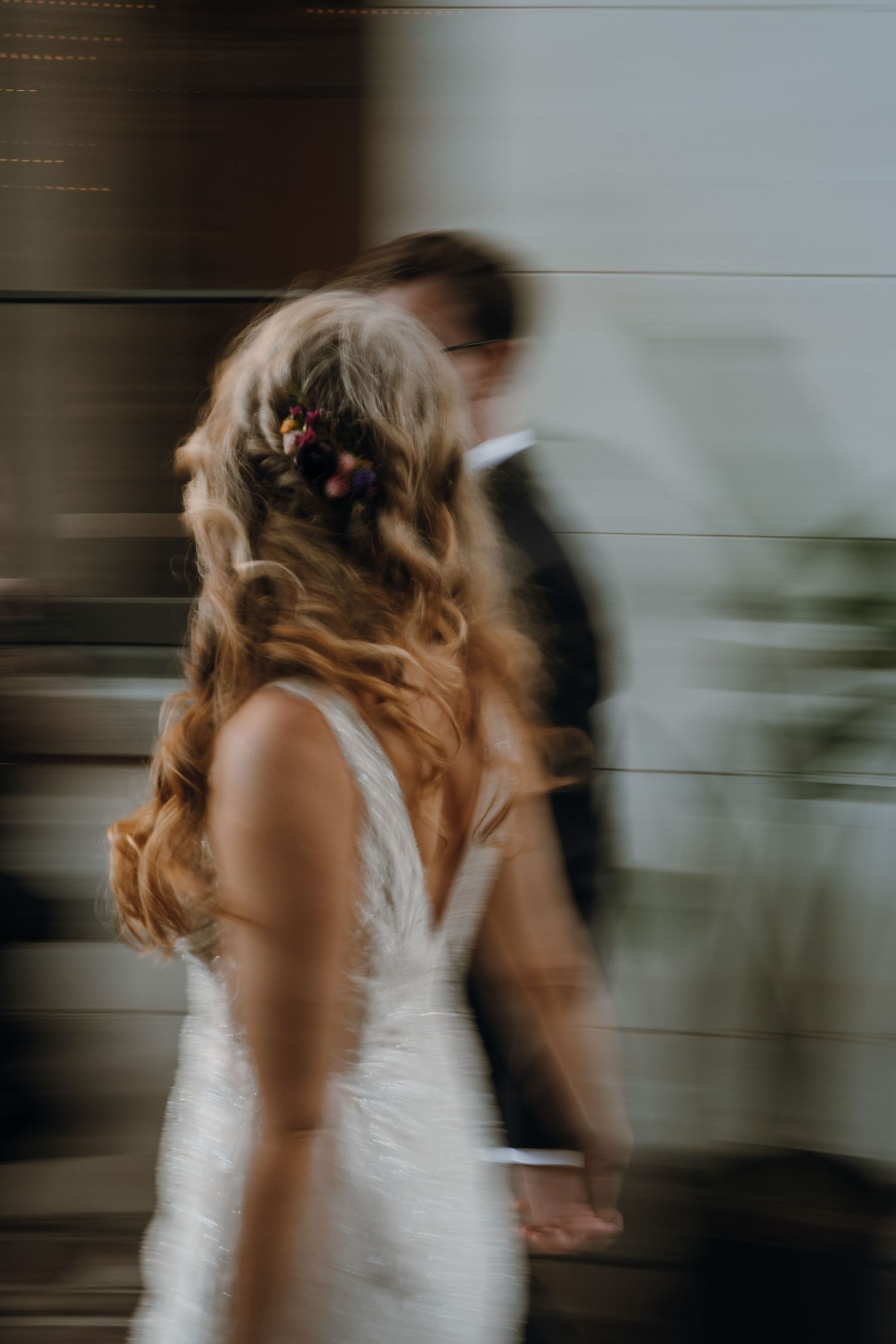 Motion blur artistic photo of bride with floral hair accessories and groom walking together.