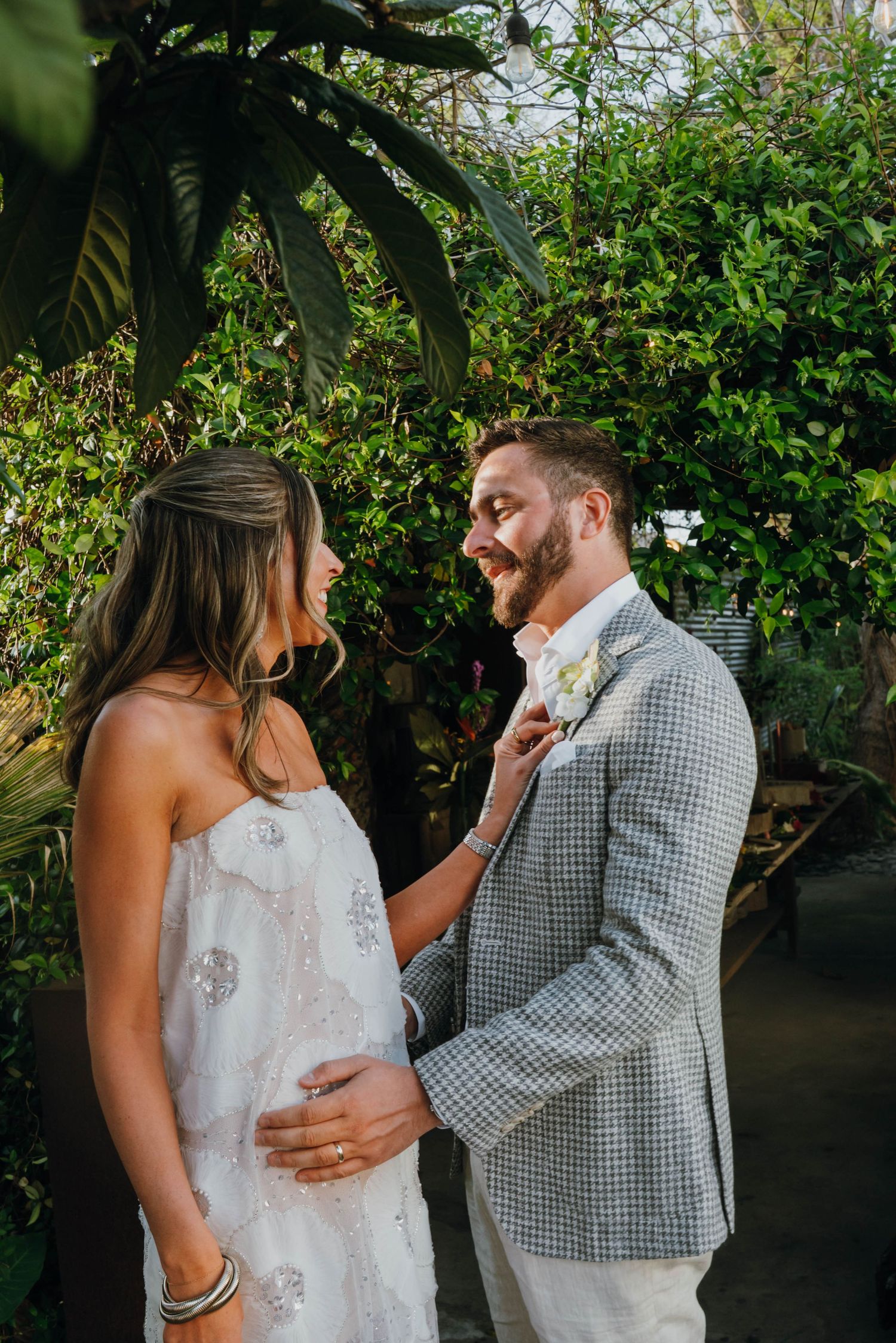Bride and groom share a tender moment, she adjusts his tie while he smiles in a grey houndstooth suit.