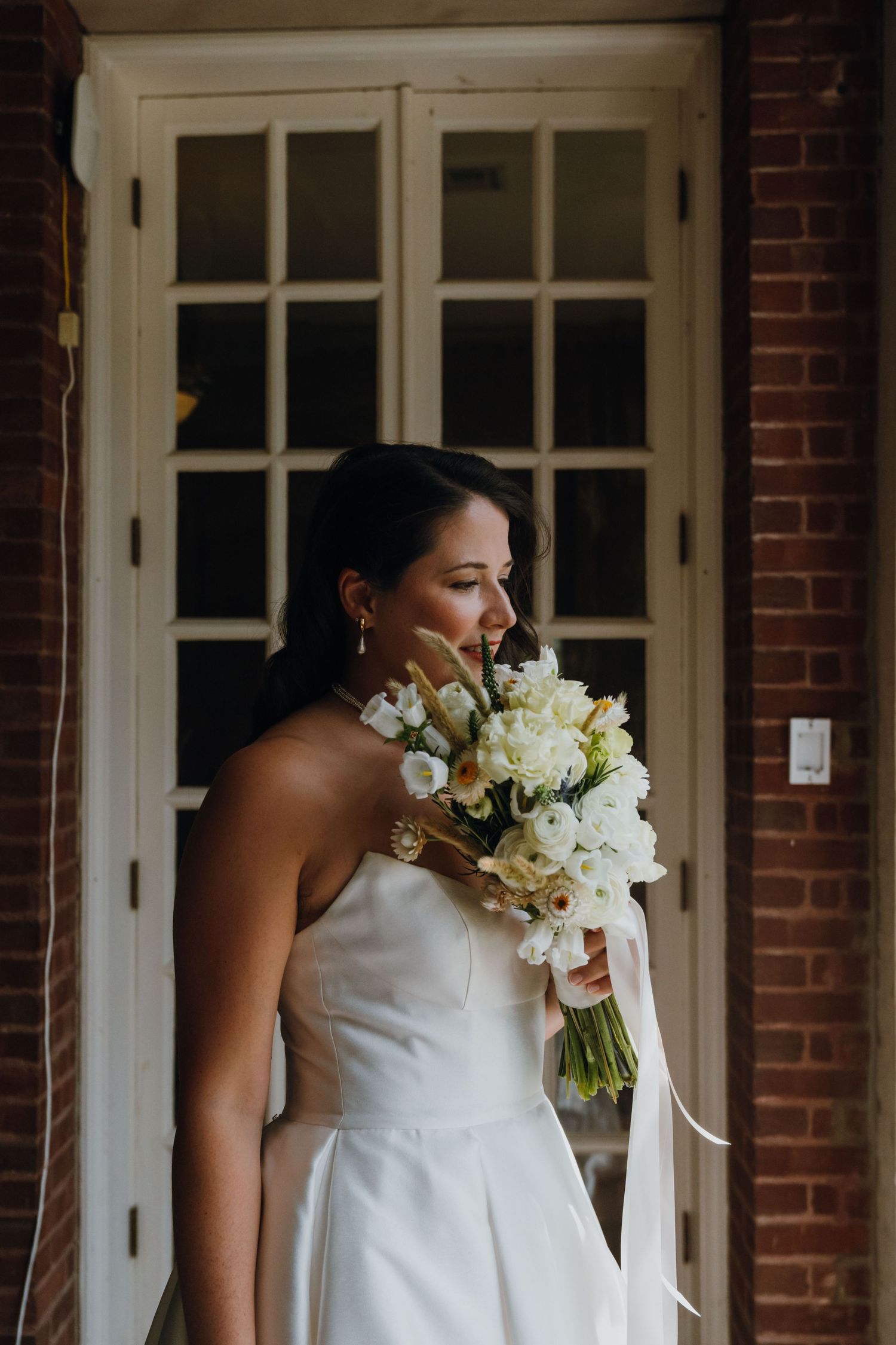 Elegant bride in strapless white gown holding white floral bouquet outside brick building. New Orleans, Louisiana, Mississippi