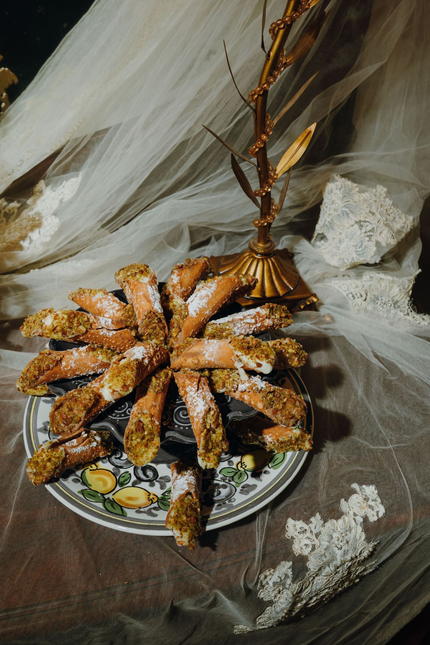 Plate of powdered sugar-dusted cannoli with pistachios arranged on decorative plate with golden candelabra.