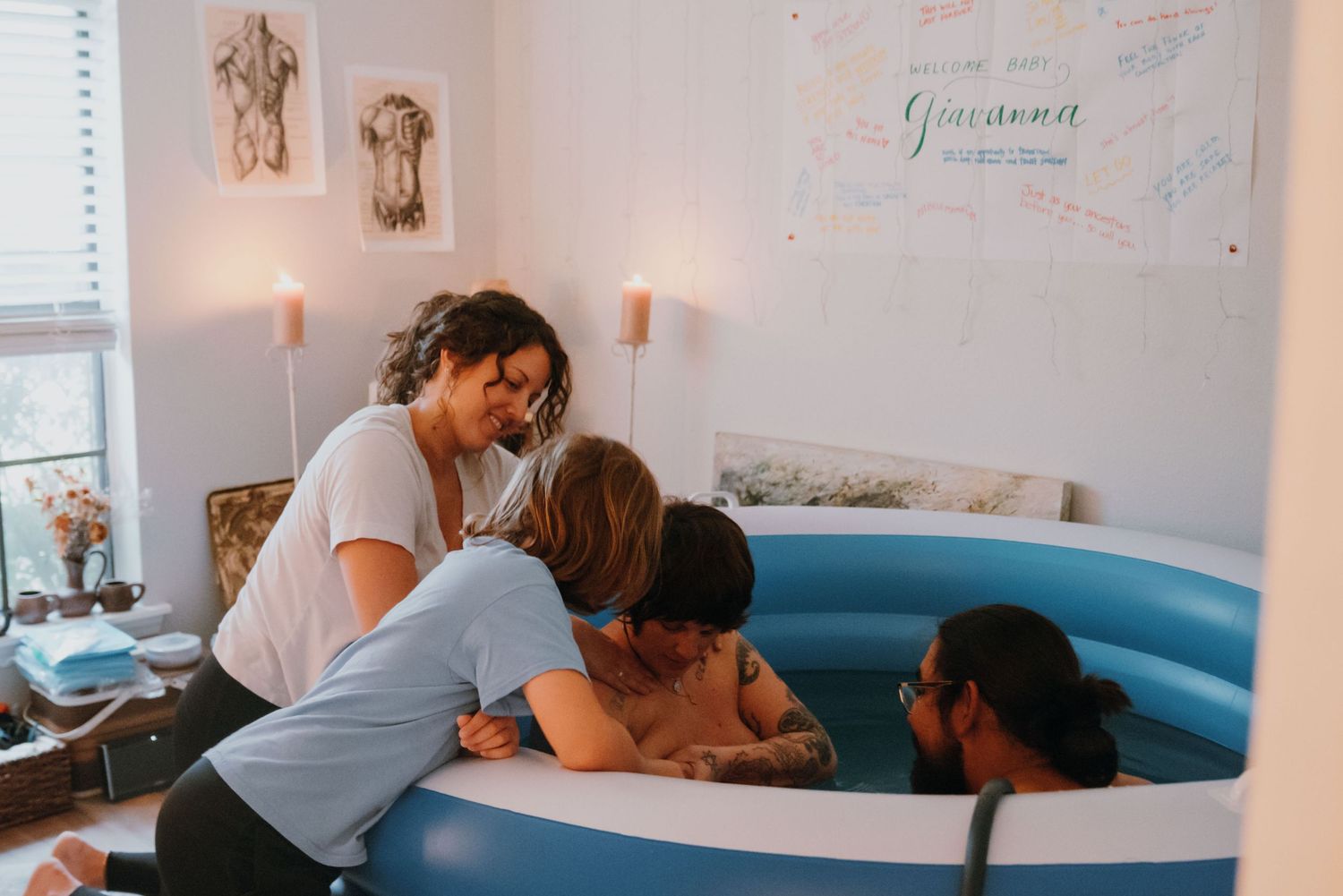 Midwife and family supporting a woman during a home water birth in a blue inflatable tub.