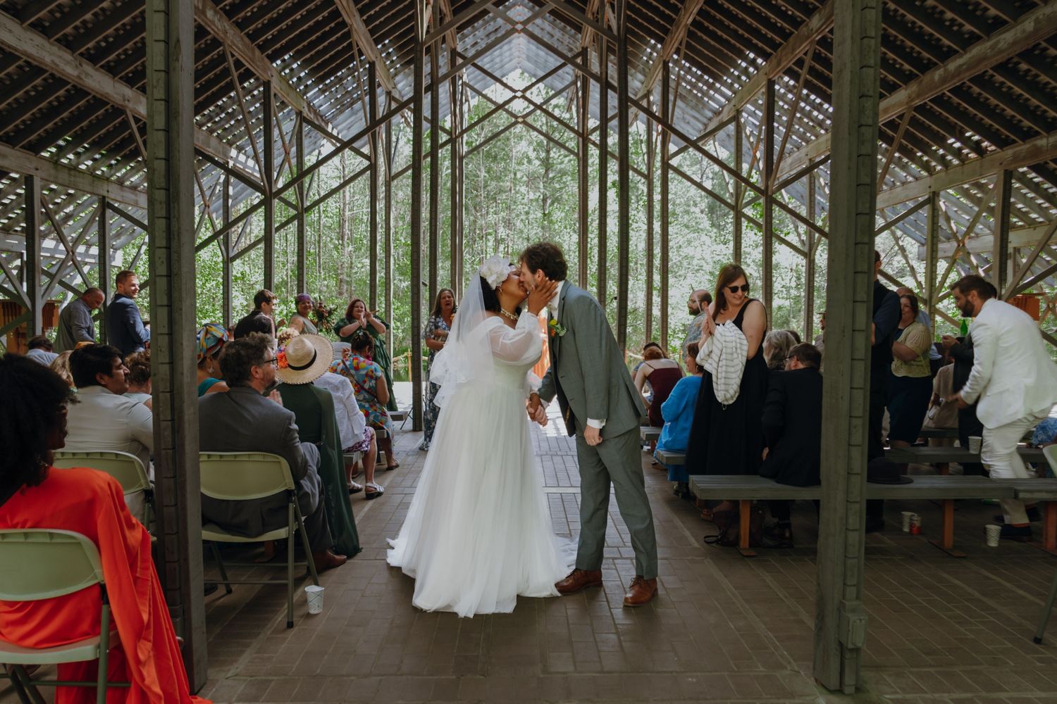 Newlyweds share first kiss at altar surrounded by guests in open-air chapel.